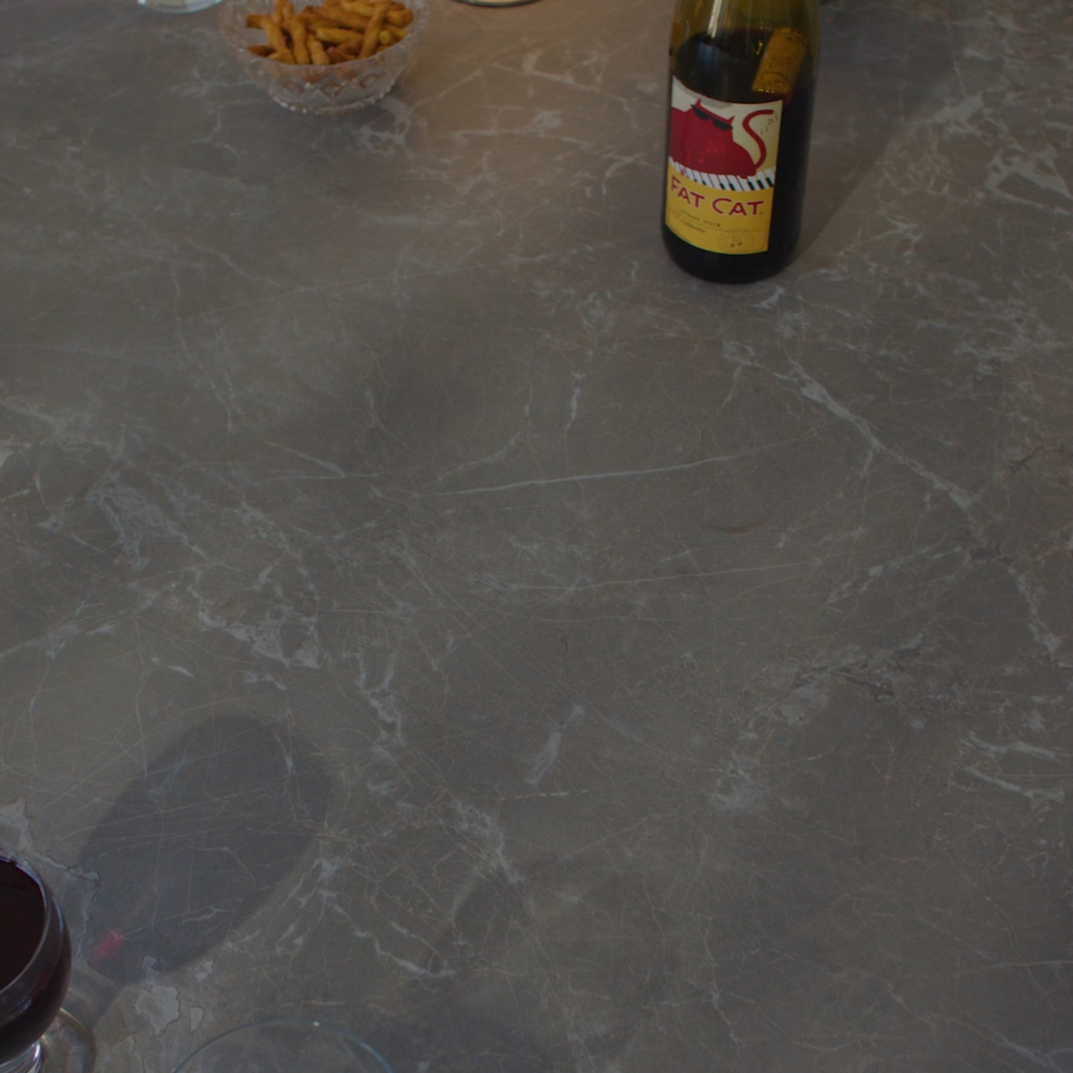 Polished gray marble surface with subtle white veining, partially showing a bottle and snack bowl on top
