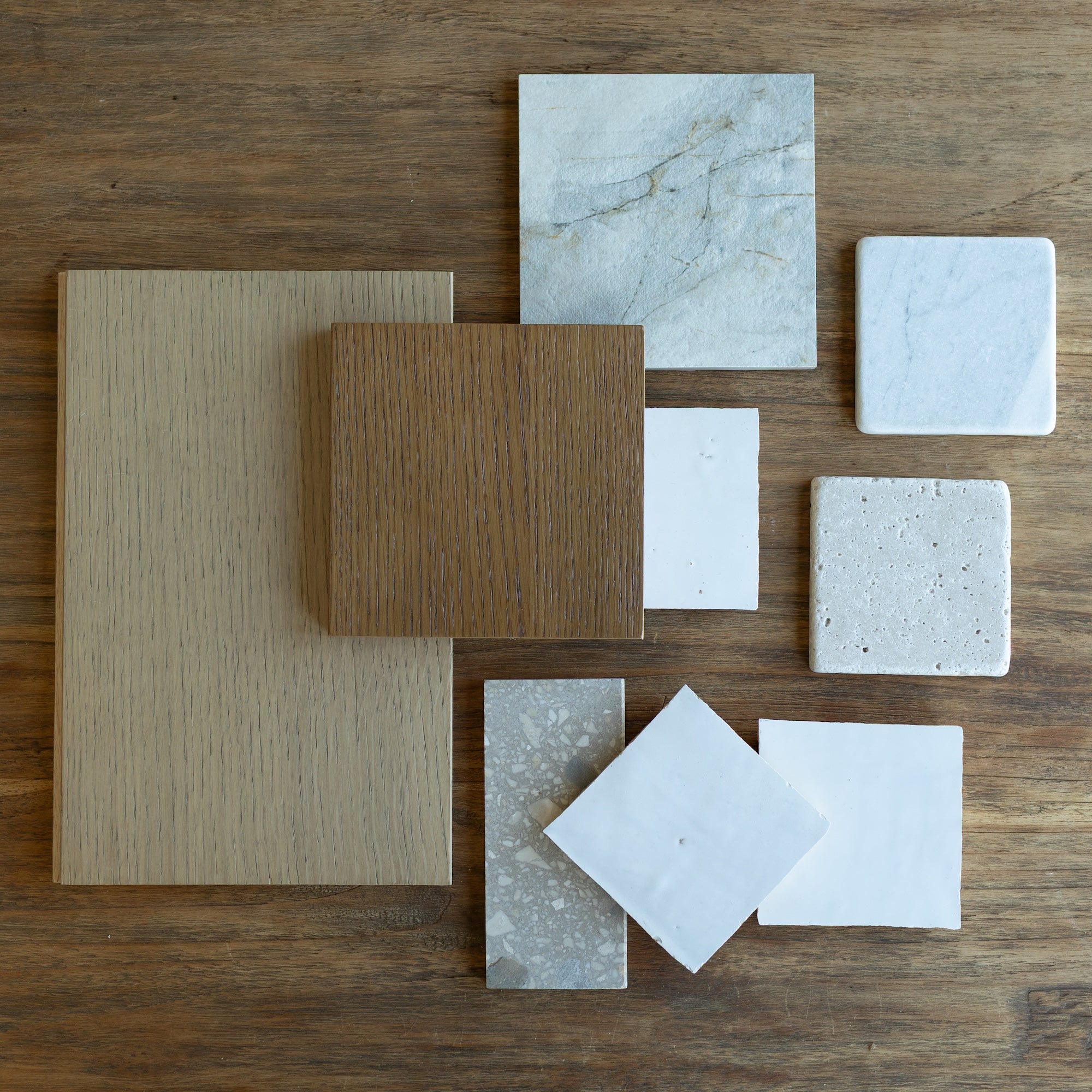 Assorted wood and stone tile samples with varied textures and neutral tones arranged on wooden background