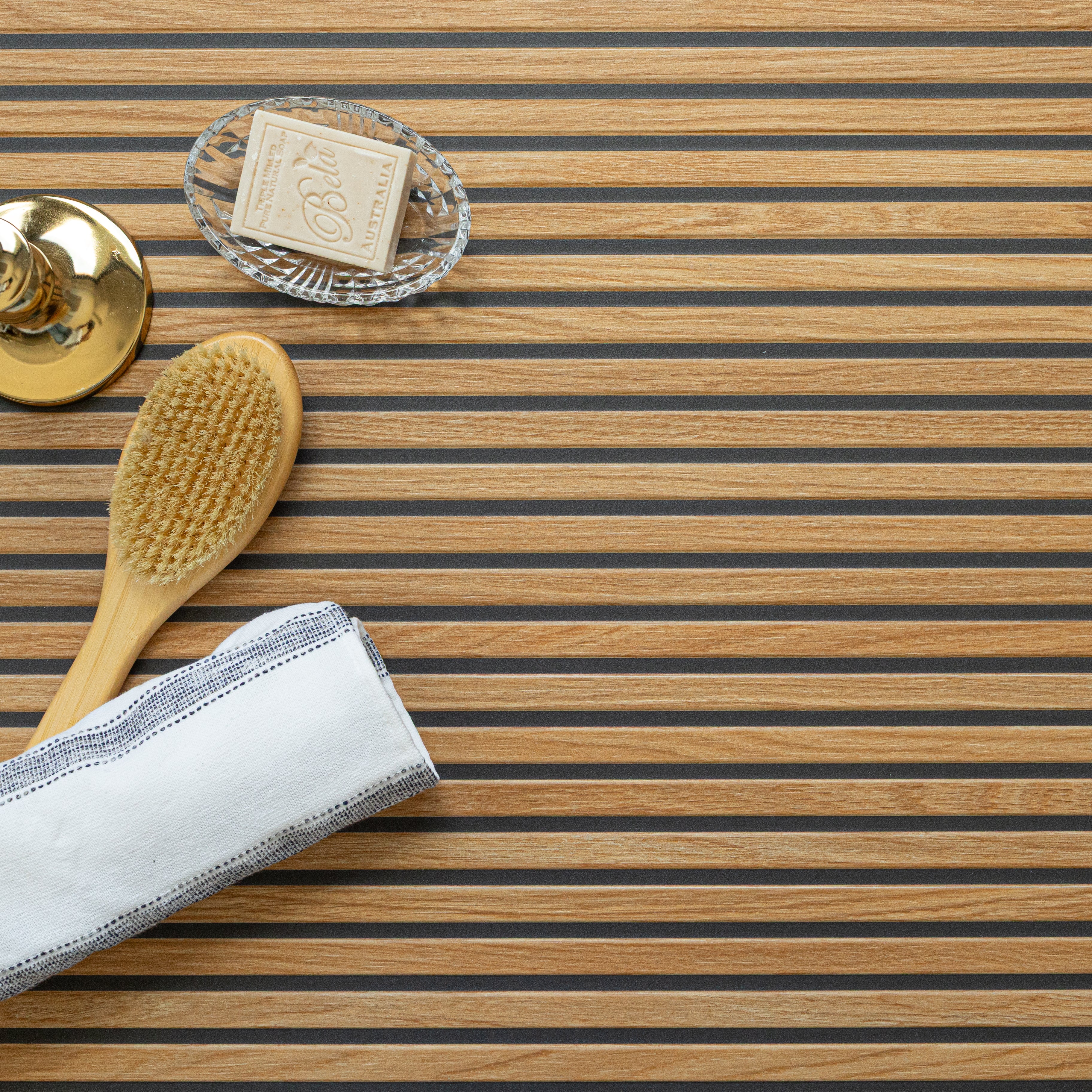 Striped wood surface with alternating light and dark wood strips, featuring a natural bristle brush, soap dish, and white towel