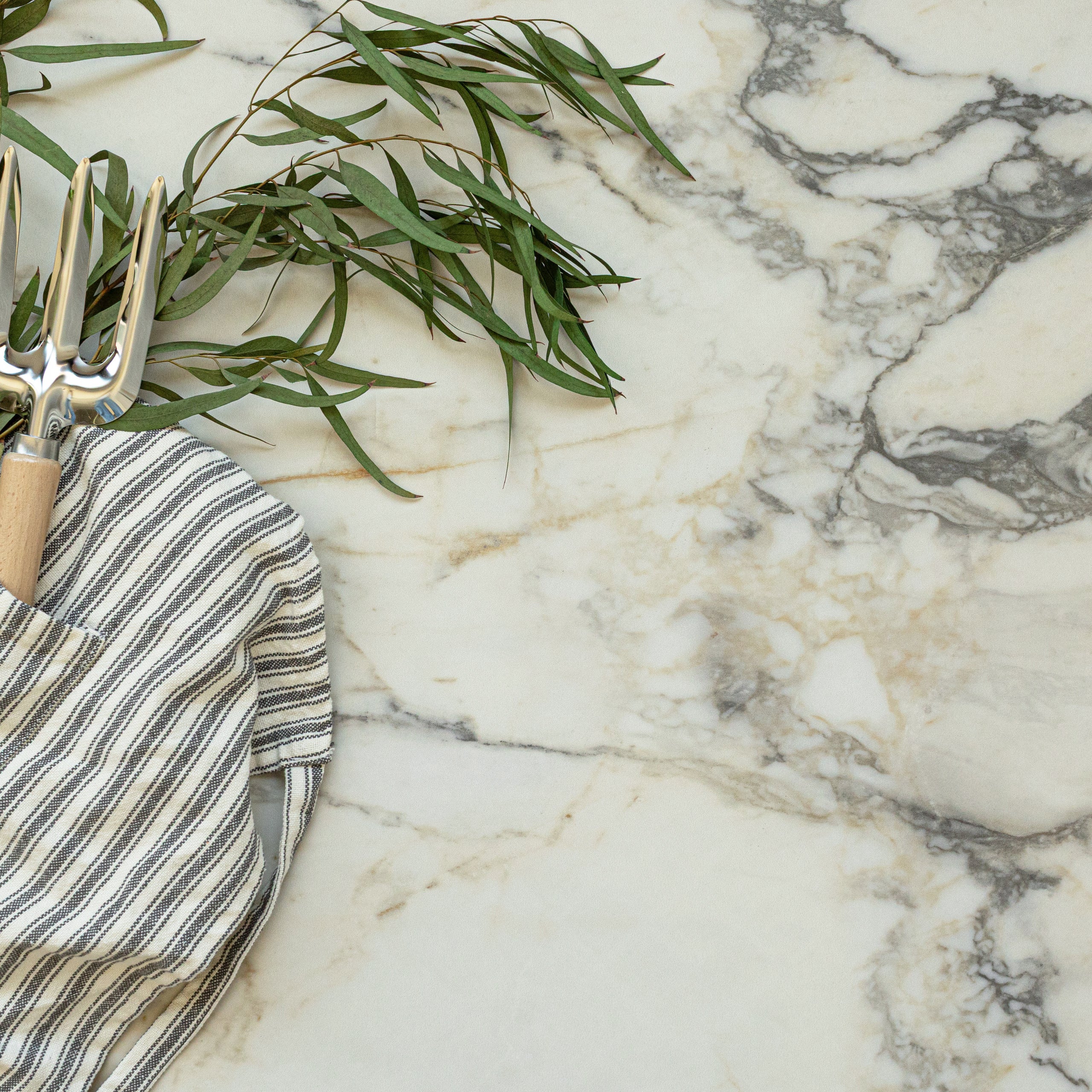 Creamy white large format tile with natural gray and beige marble veining, styled with striped linen and green foliage.