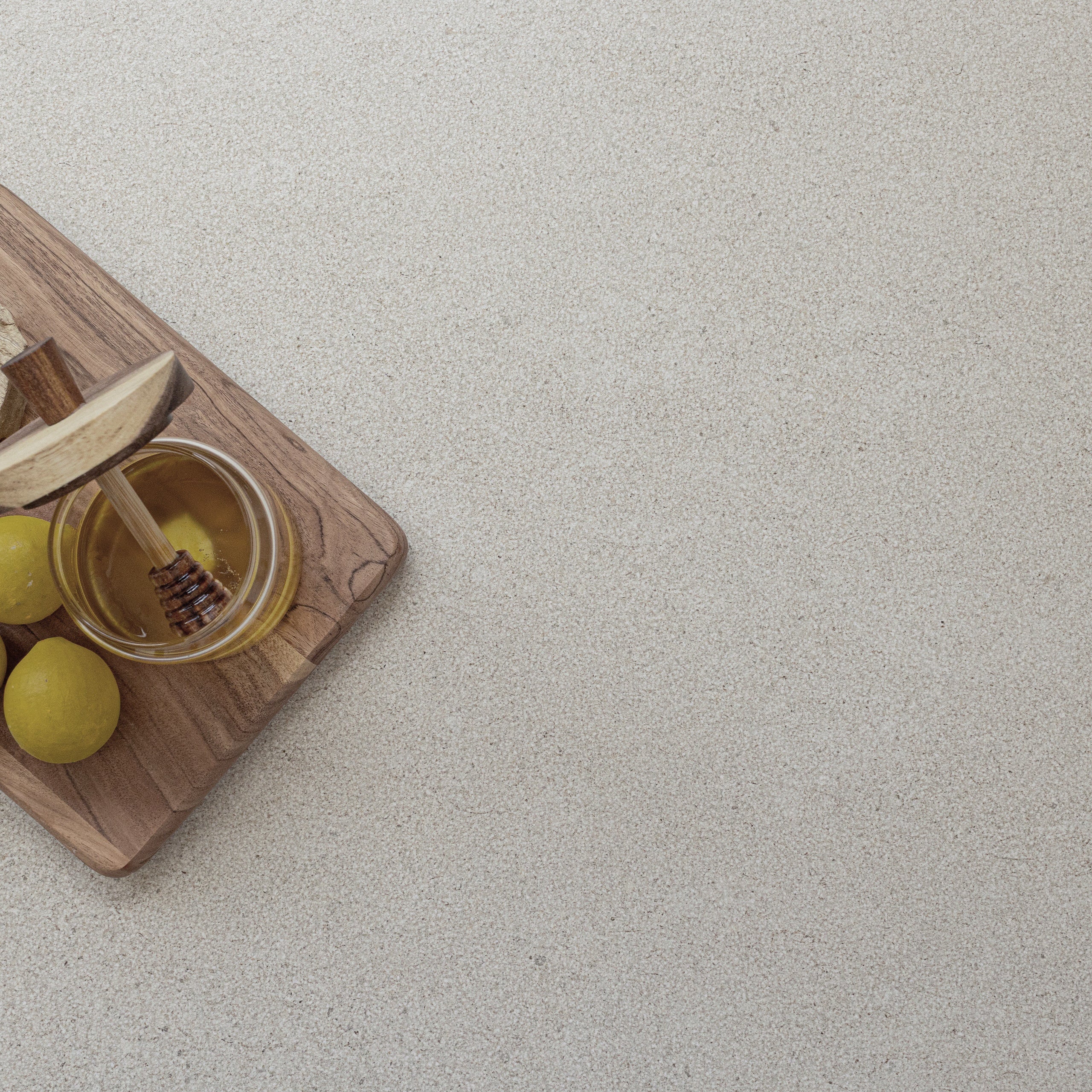Smooth porcelain tile surface in soft almond hue with subtle limestone-inspired texture and wooden board with honey and lemons in corner