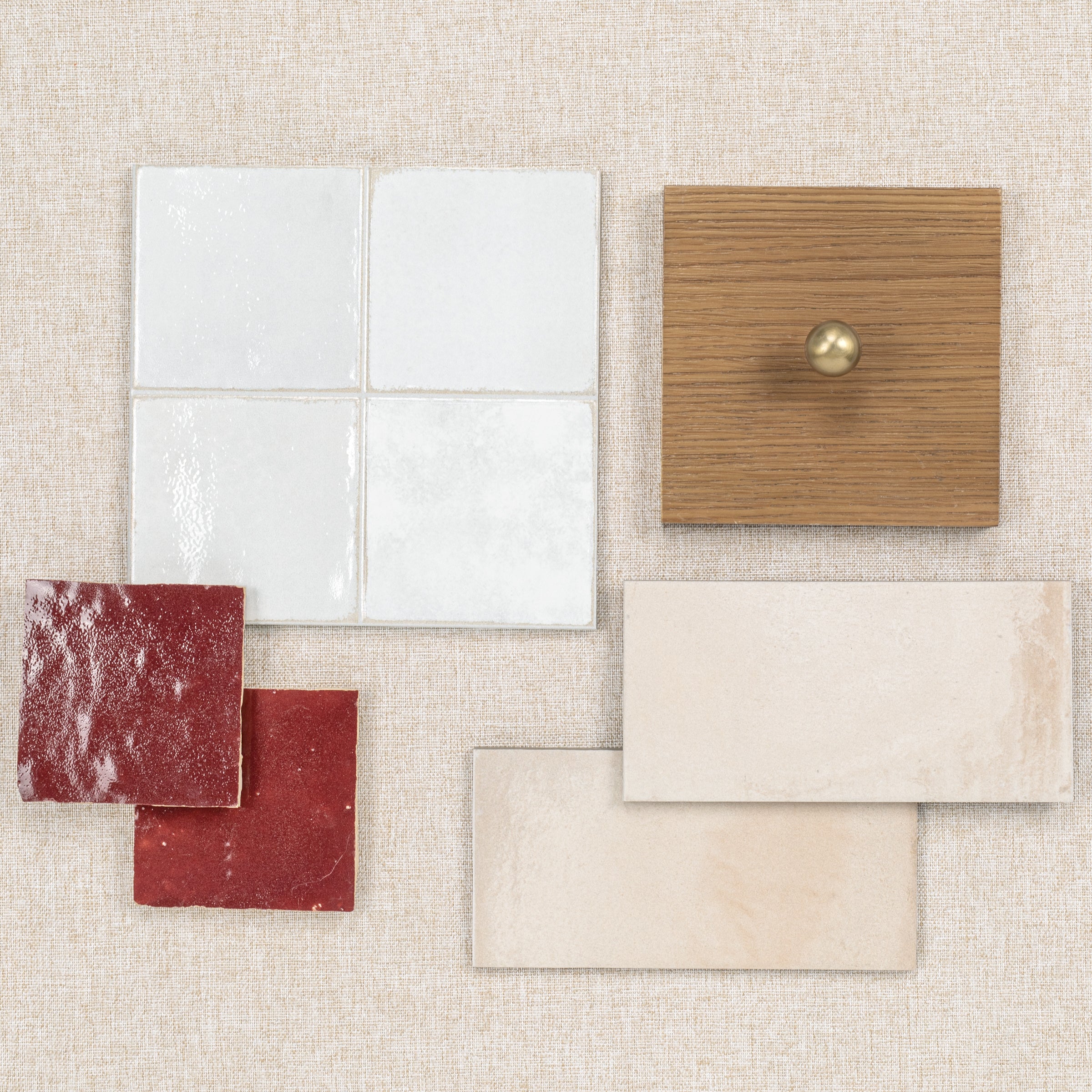 Various ceramic and porcelain tile samples alongside a wood sample with a brass knob on textured fabric background