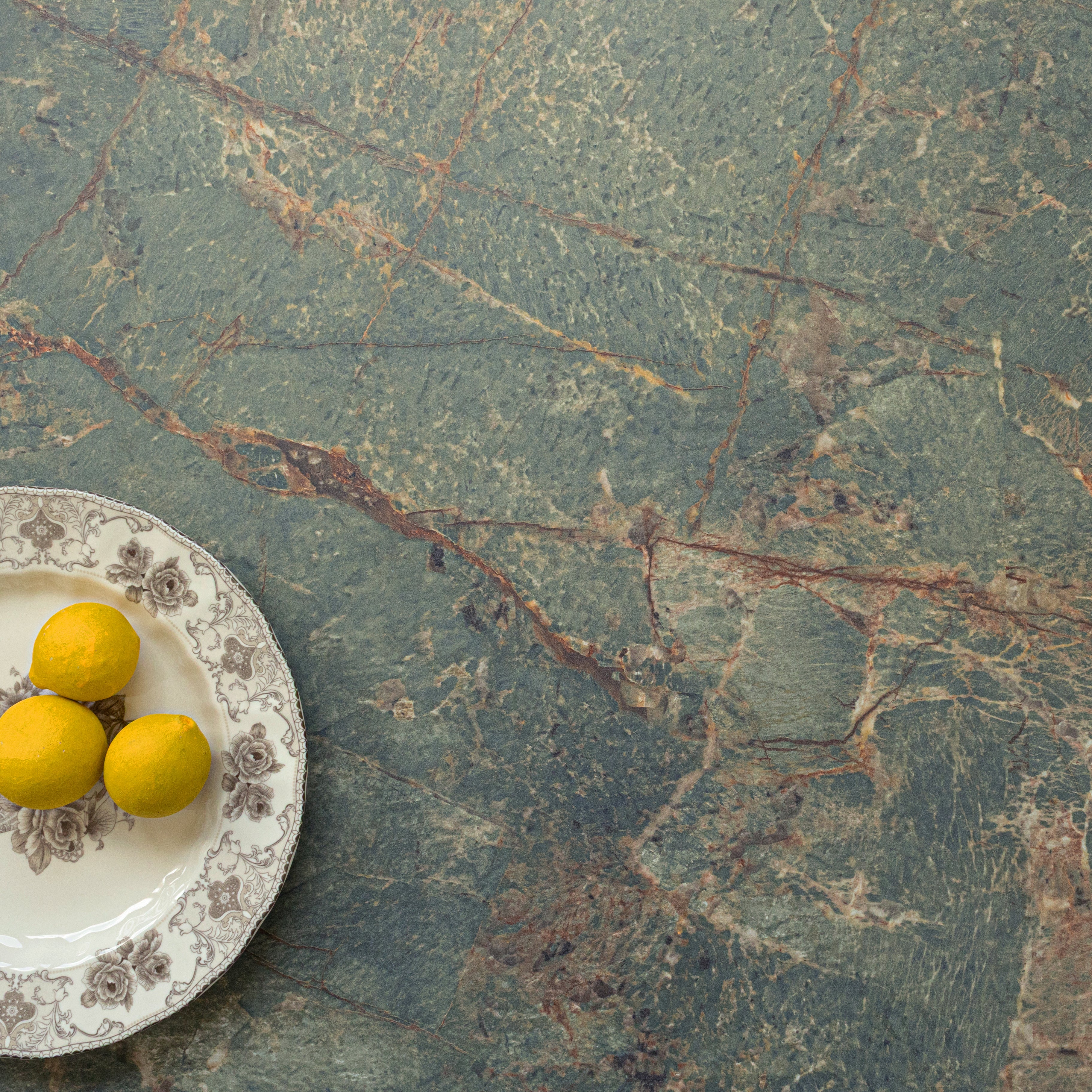 Matte green porcelain tile surface with natural stone texture beside a vintage plate holding three yellow lemons