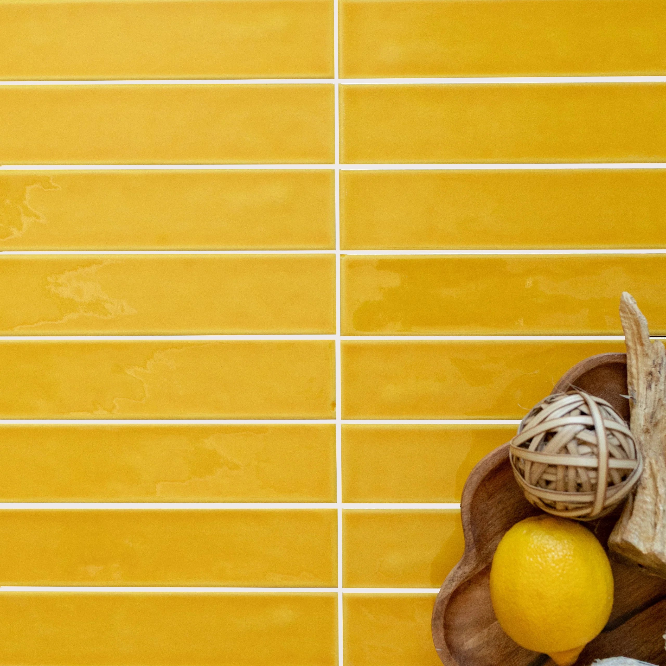 Glossy amber ceramic tiles laid horizontally with a wooden bowl holding a lemon and decorative natural elements