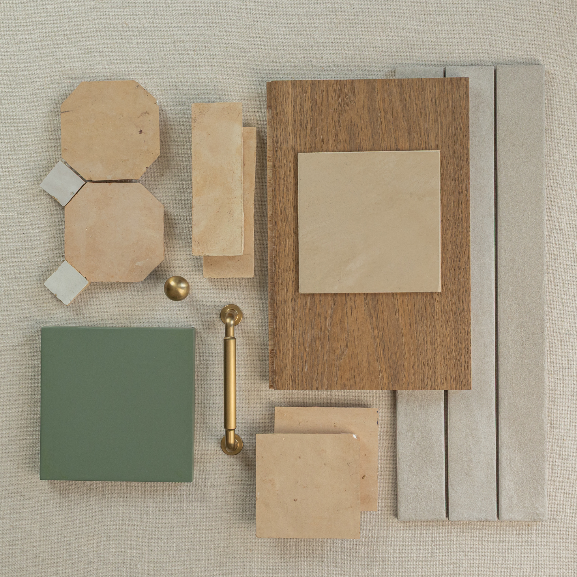 Top view of ceramic tile samples in beige, green, wood texture, and brass hardware on a neutral fabric background