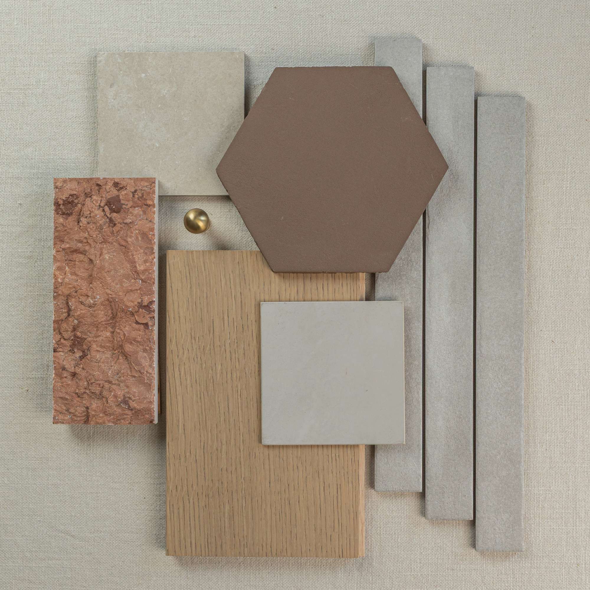 Flat lay of ceramic tiles, wood and stone samples in beige, brown, and gray tones with a brass knob on fabric background
