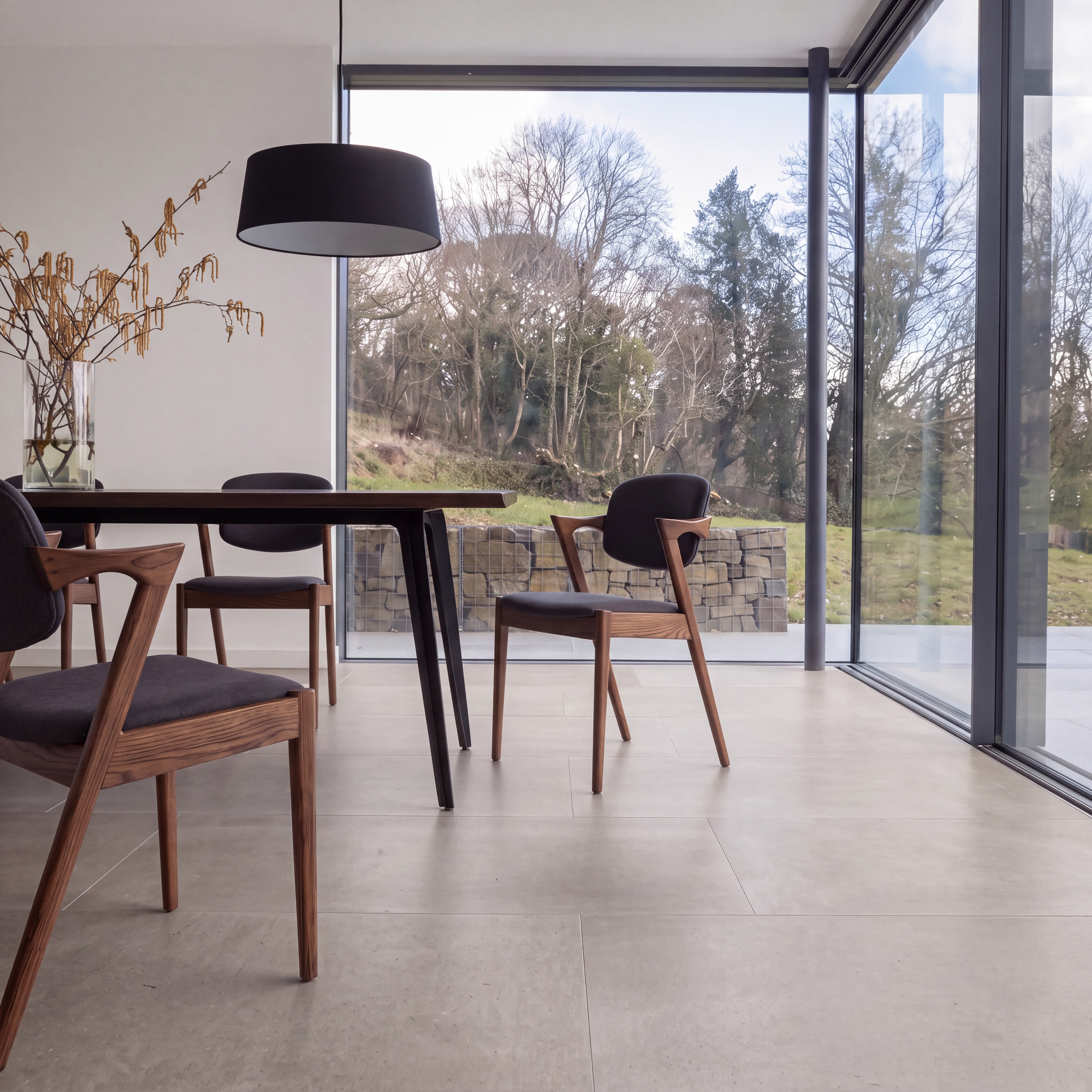 Modern dining room with large format tile flooring, wood chairs, table, and windows overlooking a garden