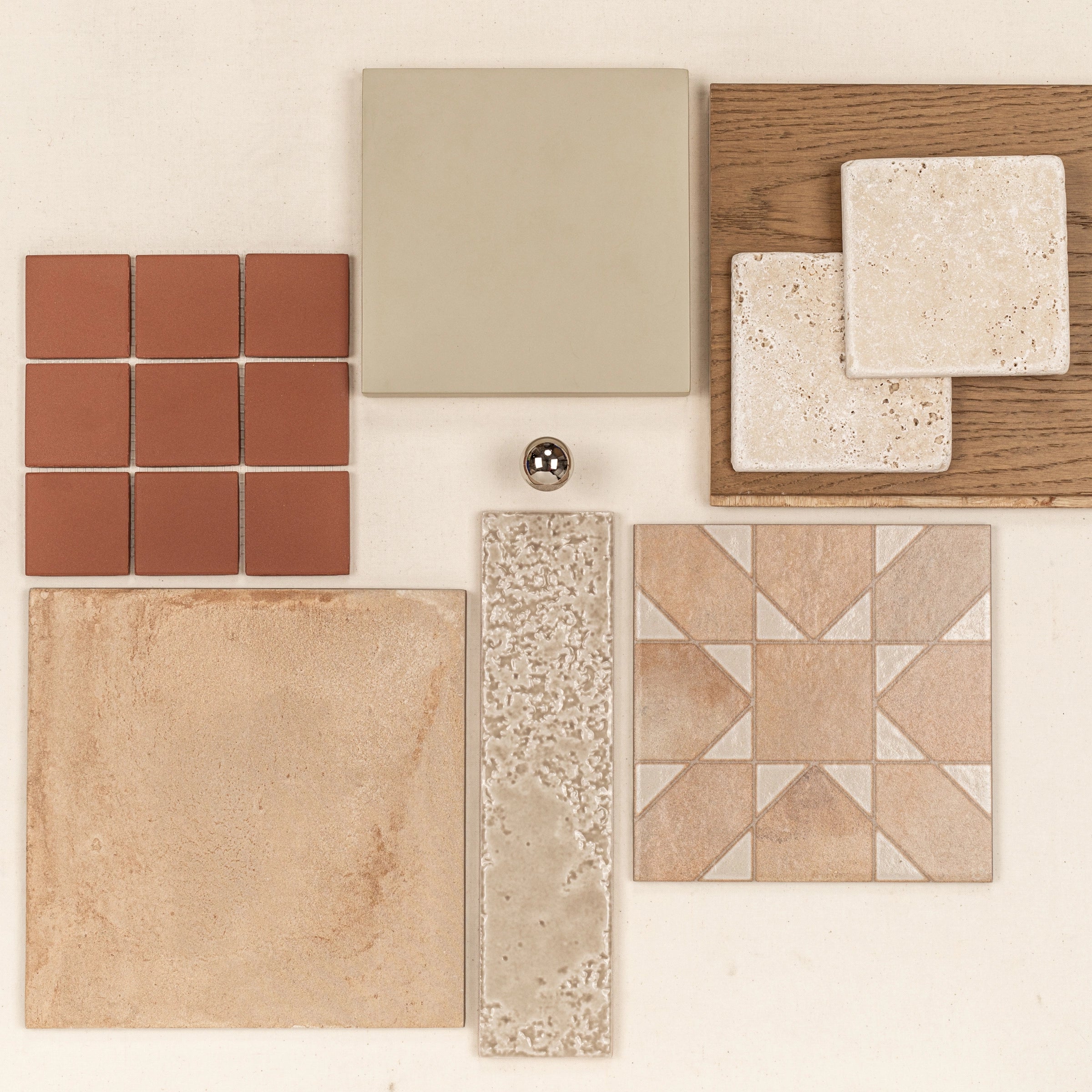 Assorted natural and ceramic tiles with wood and metallic accents in warm earthy and neutral tones arranged on a light background
