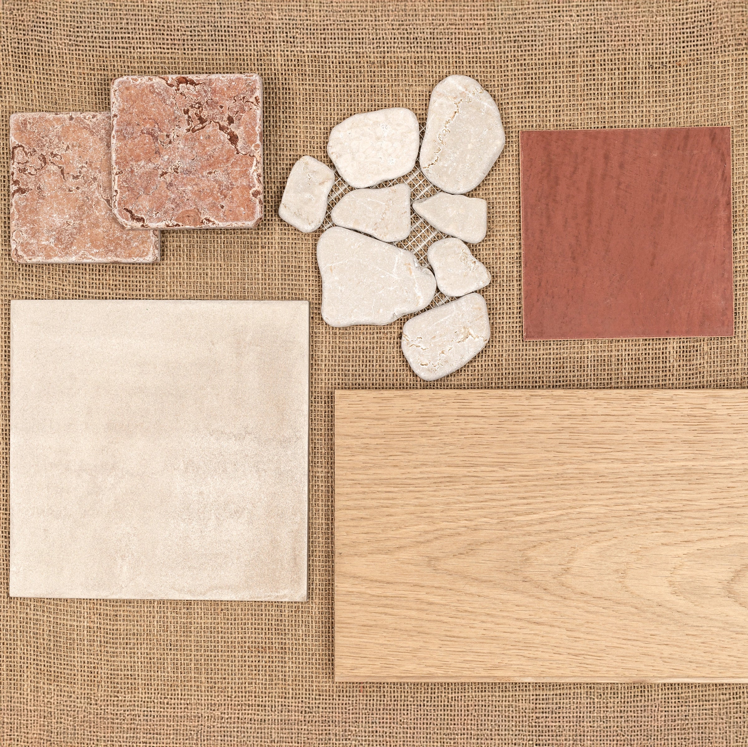 Variety of textured ceramic tiles, natural stone pieces, and a wood plank sample arranged on a woven fabric background