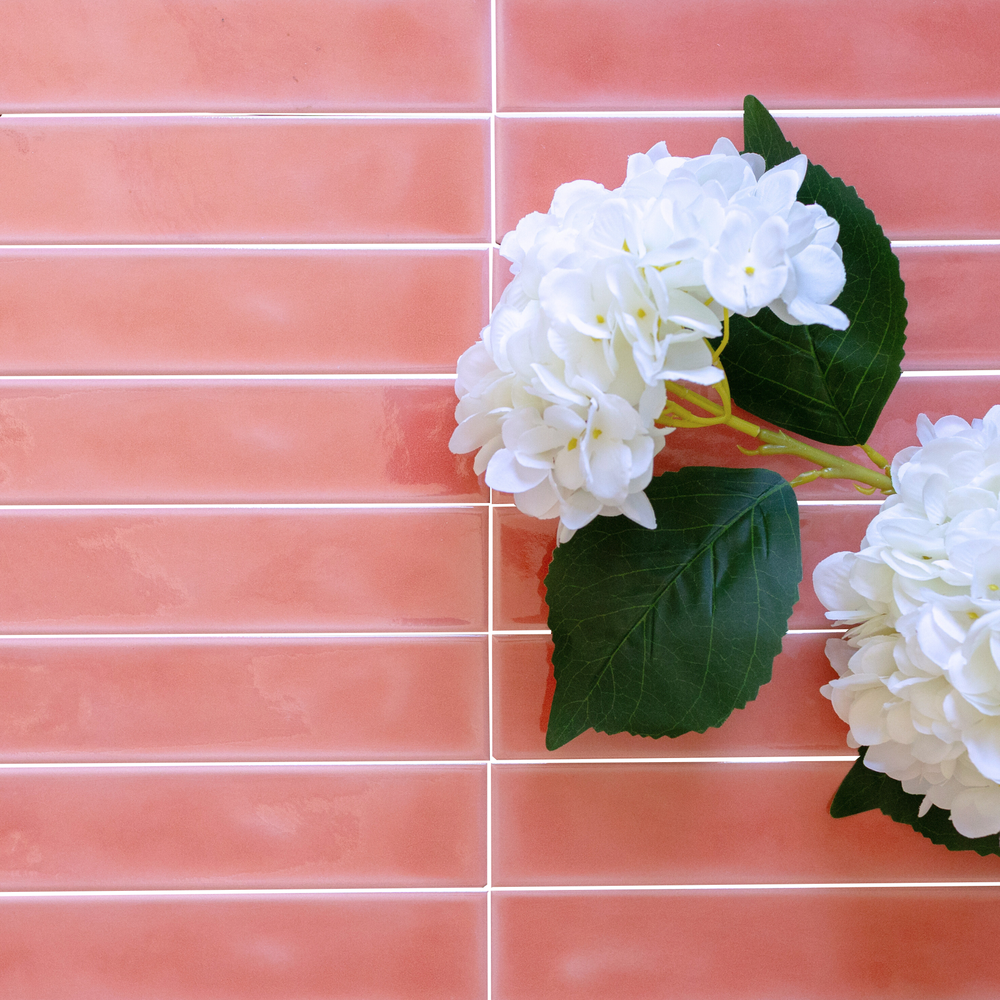 Glossy rectangular ceramic tiles in warm coral tones with white hydrangea blooms and green leaves nearby
