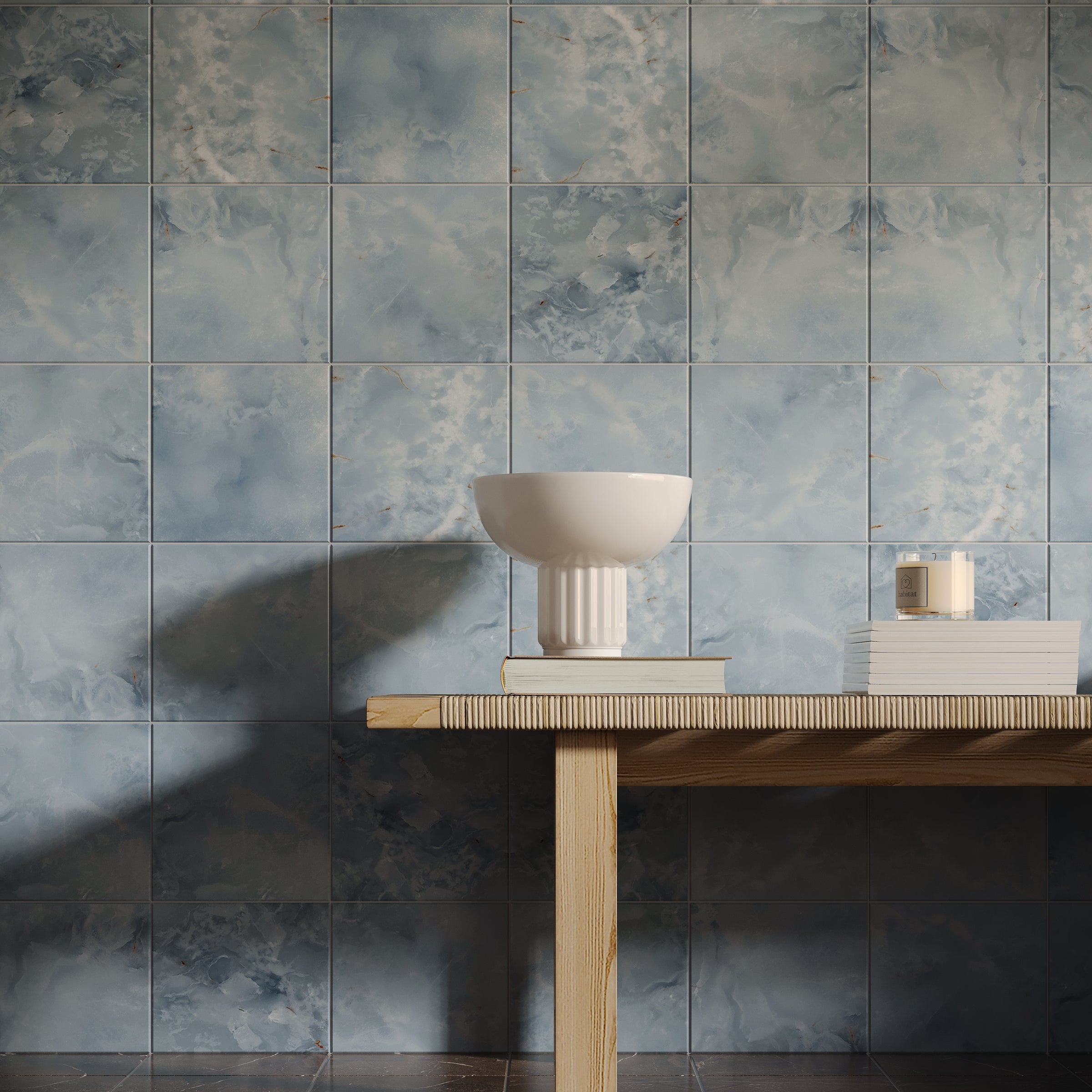 Matte blue ceramic tiles with cloudy textured patterns forming a soft, nature-inspired backdrop behind a wooden table with decor items