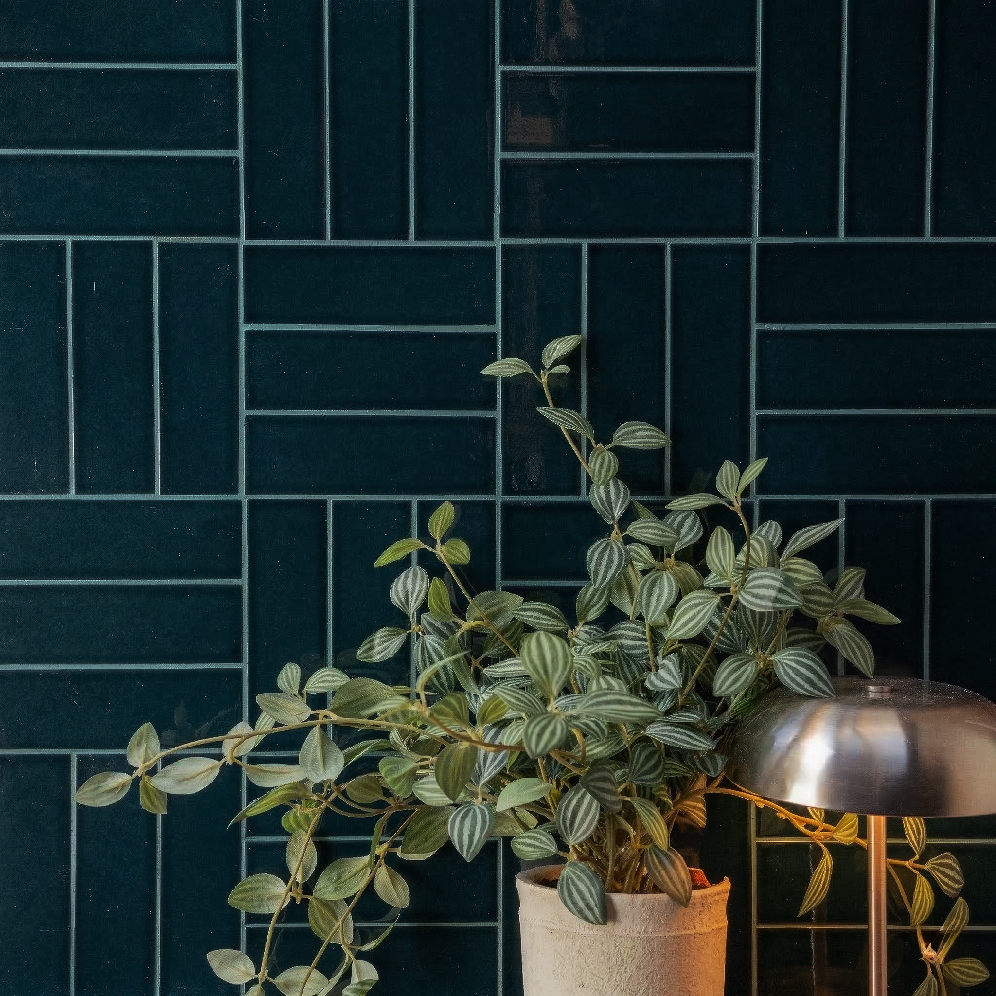 Dark teal ceramic tiles in an interlocking pattern with a potted trailing plant and a metallic lamp nearby