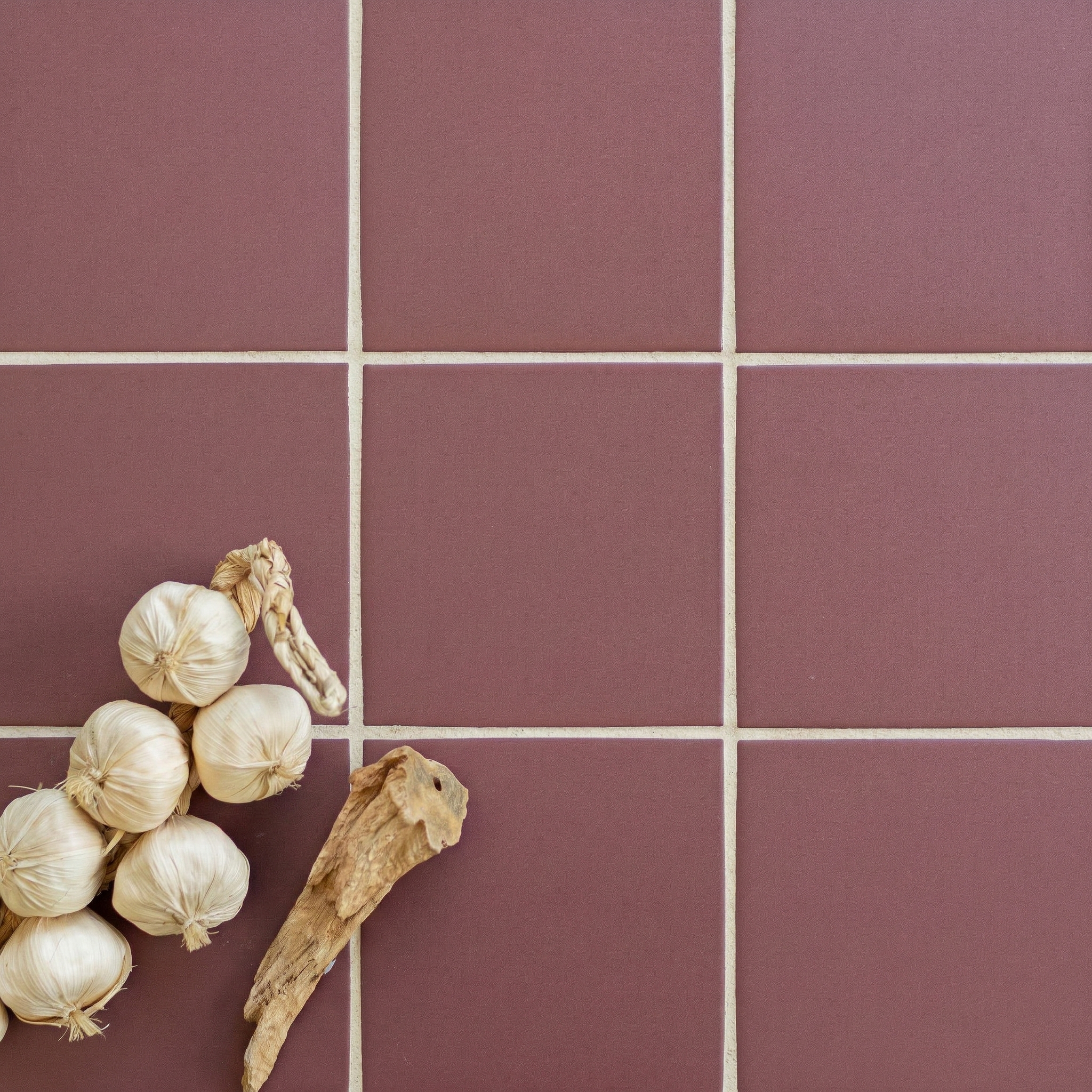 Matte maroon ceramic tile flooring with beige grout and decorative garlic and dried root accents on the corner