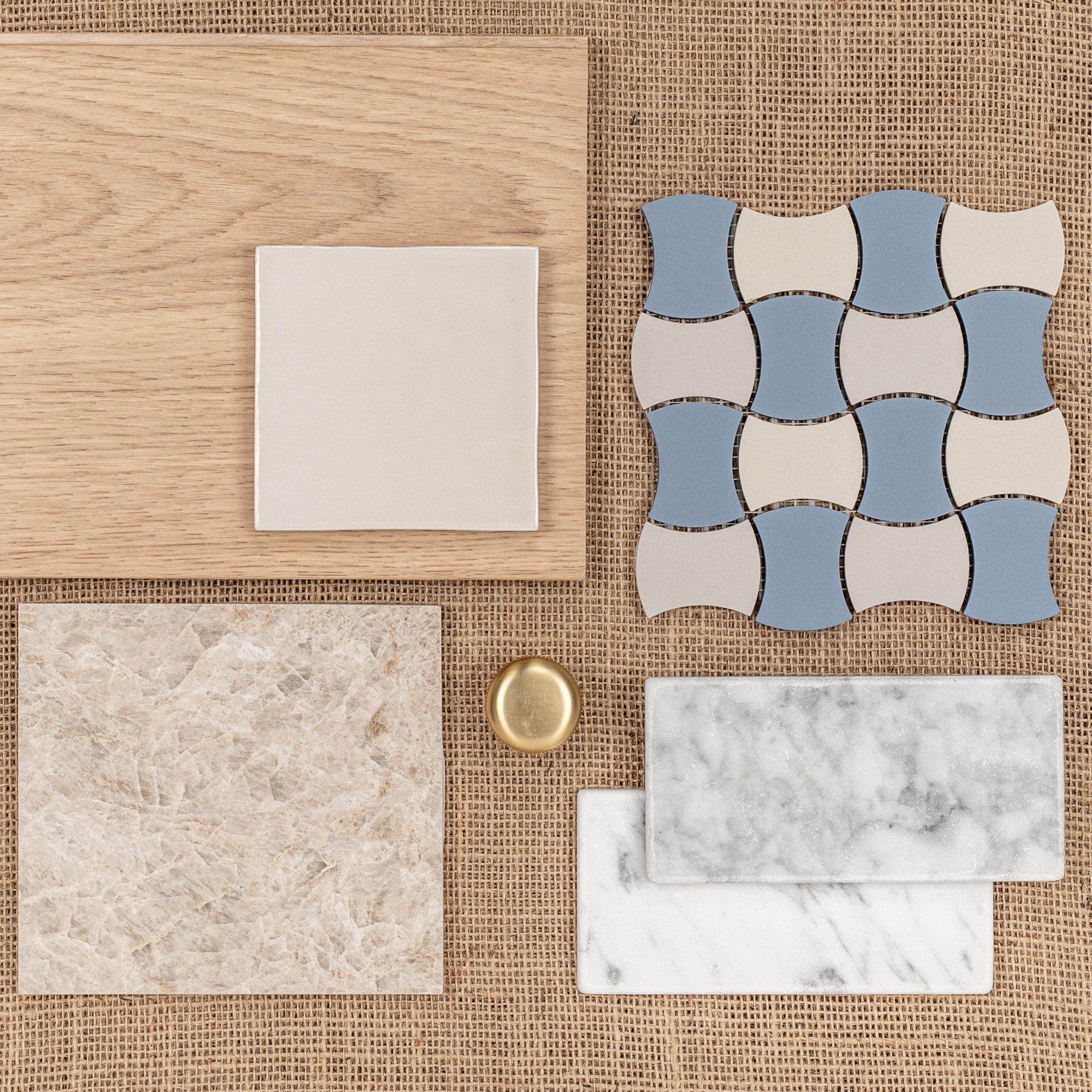 Assorted tile and wood samples in natural beige, blue, and marble patterns arranged on woven fabric with a brass knob
