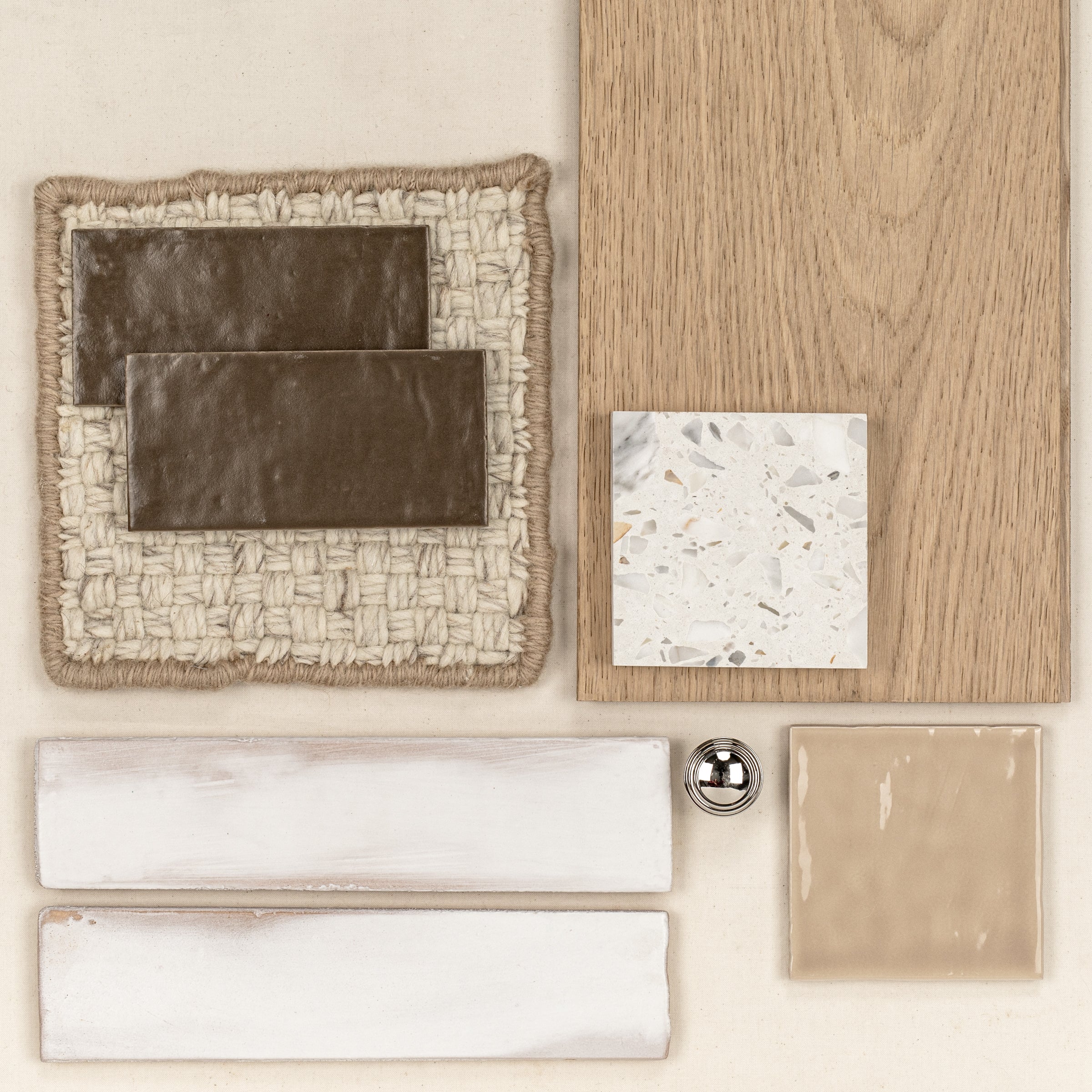 Two dark brown rectangular ceramic tiles on woven fabric next to wood-look flooring and terrazzo tile sample with neutral ceramic tiles and metal knob