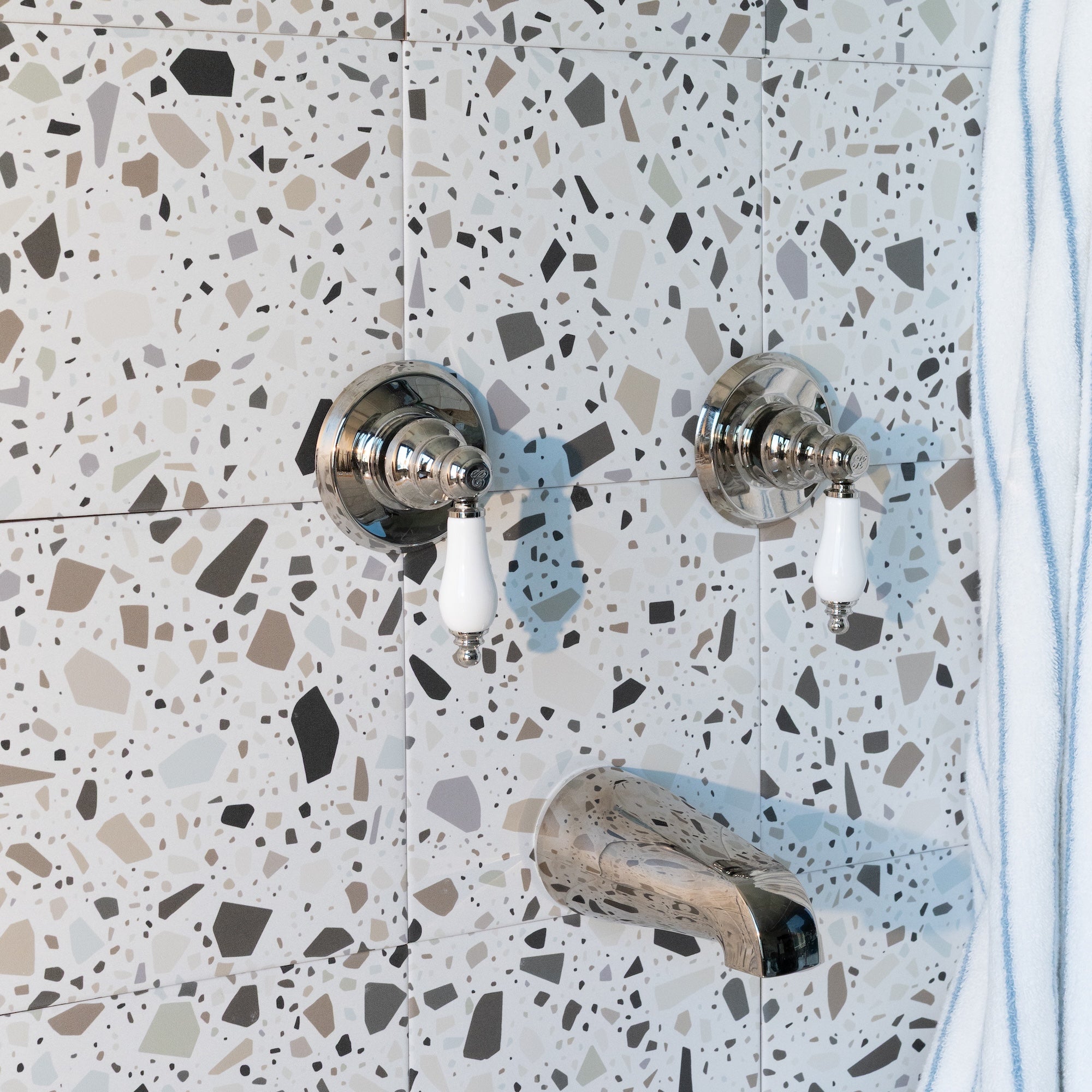 Terrazzo ceramic tiles with black, beige, and gray chips featuring chrome and white shower controls and spout.