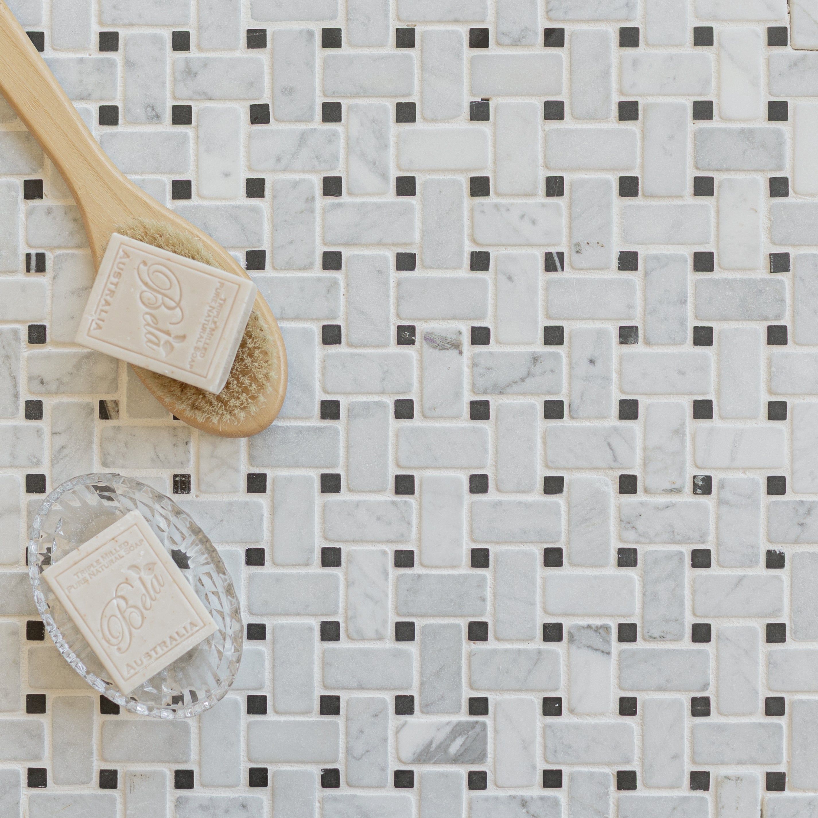 Basketweave marble mosaic tiles in soft white and gray tones with natural soap bars and a wooden bath brush nearby