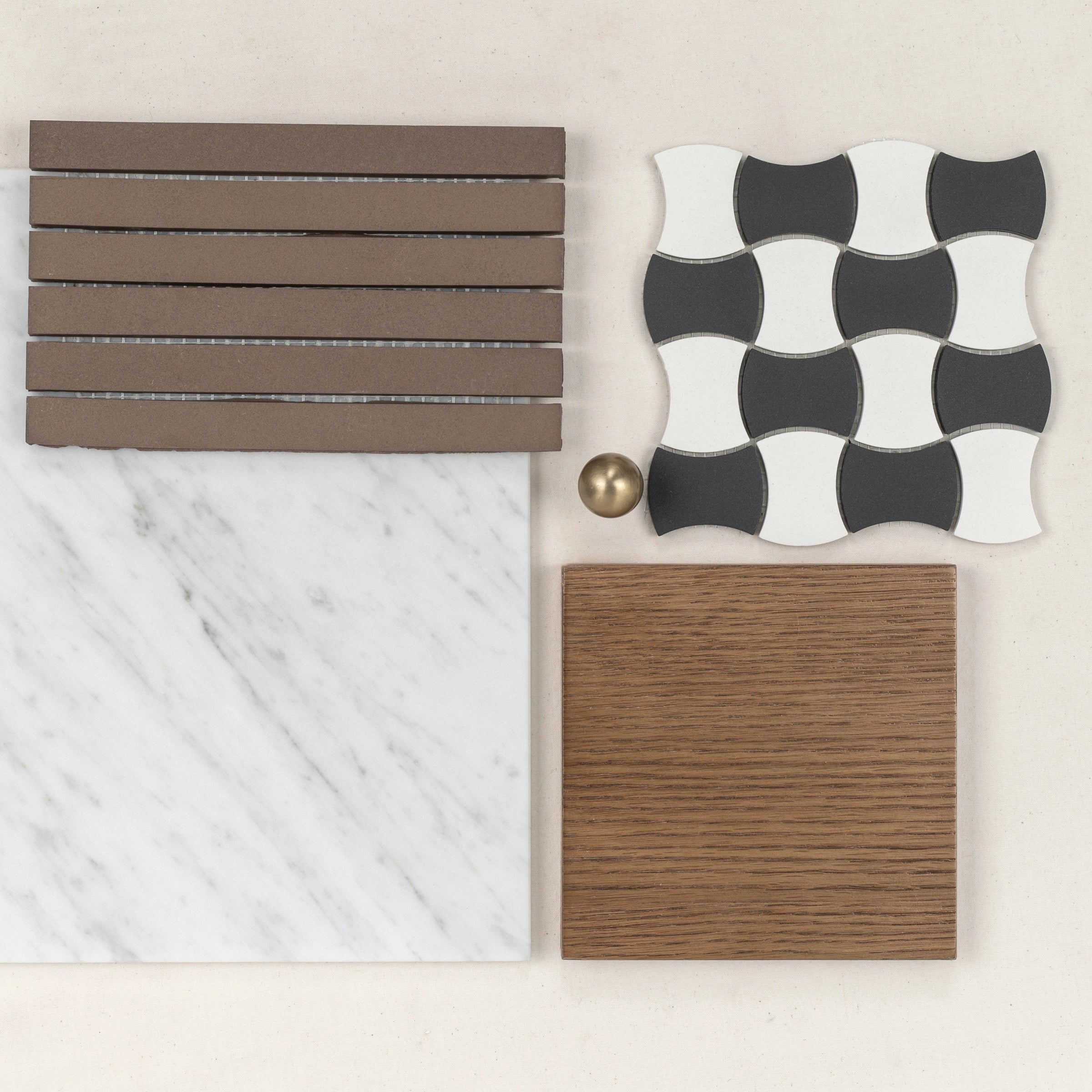 Selection of marble, wood, curved black and white tiles, and matte brown rectangular tiles with brass accent ball on light background