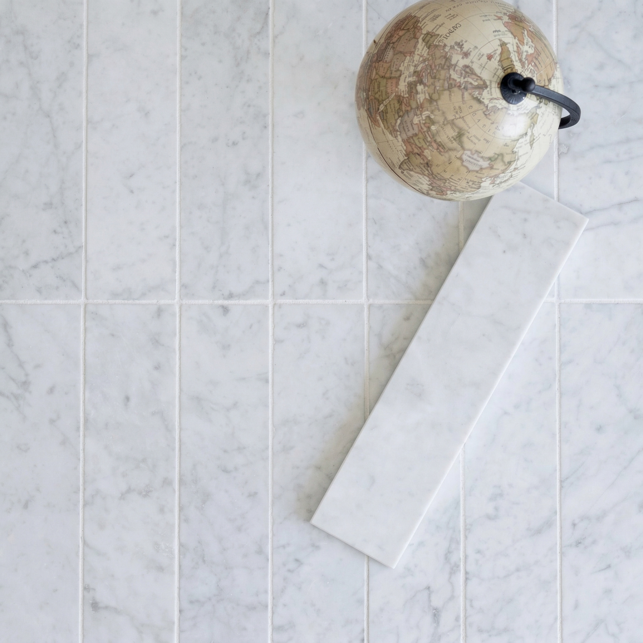 White marble-look ceramic tiles with subtle gray veining laid in a staggered pattern beside a small vintage globe
