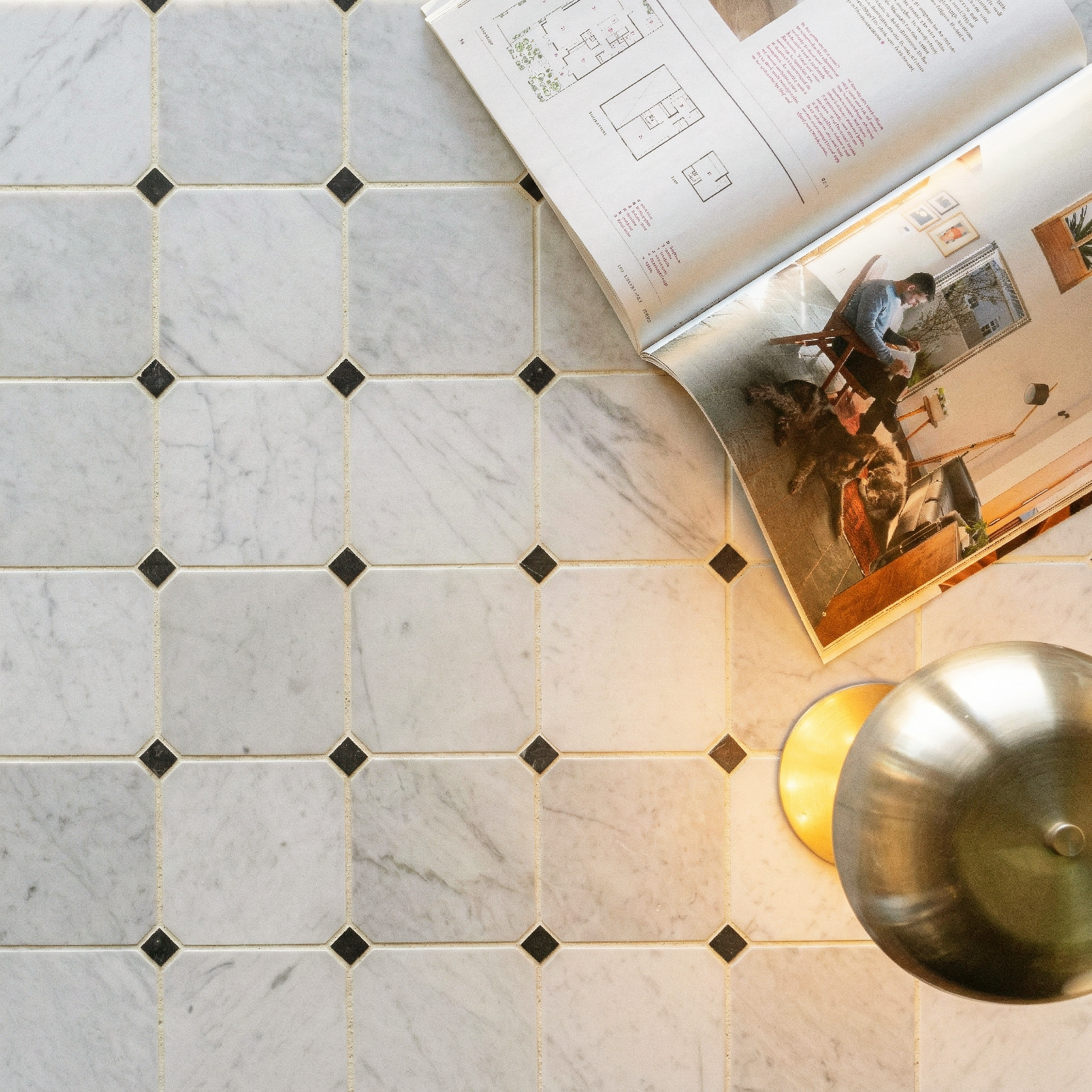Light gray marble-look tiles with small dark diamond accents beside an open magazine and metallic table lamp light