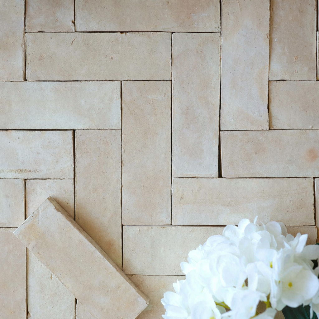 Top-down view of cream ceramic tiles arranged in a herringbone pattern with a cluster of white flowers nearby