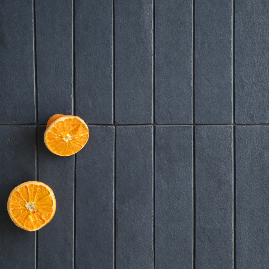 Overhead view of rectangular dark gray porcelain tiles with two halved bright orange fruit pieces nearby