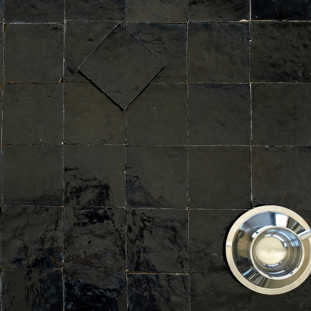 Glossy black ceramic tiles arranged in a grid pattern with a shiny silver cup and spoon on the corner