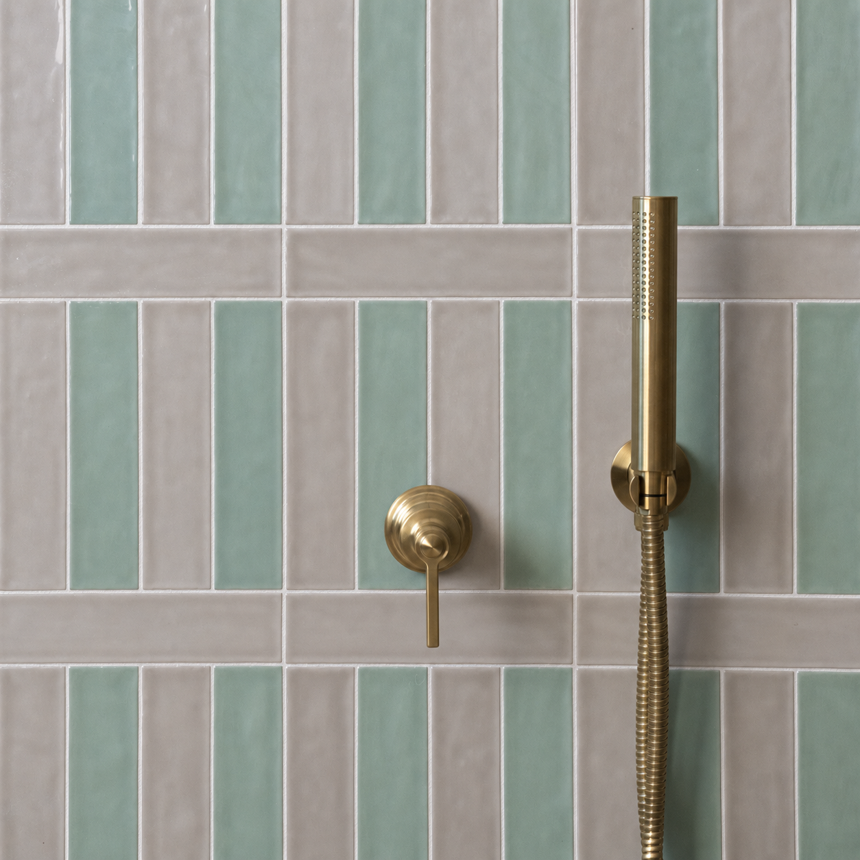 Green and gray rectangular tile wall with a brass handheld shower fixture