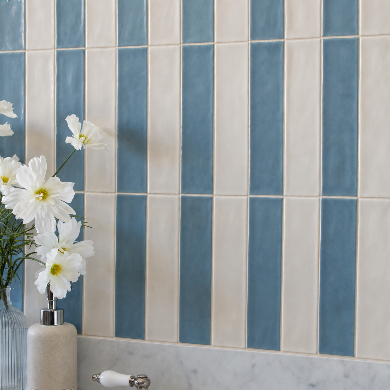 Blue and white vertical ceramic tile wall with white flowers beside a marble vanity top
