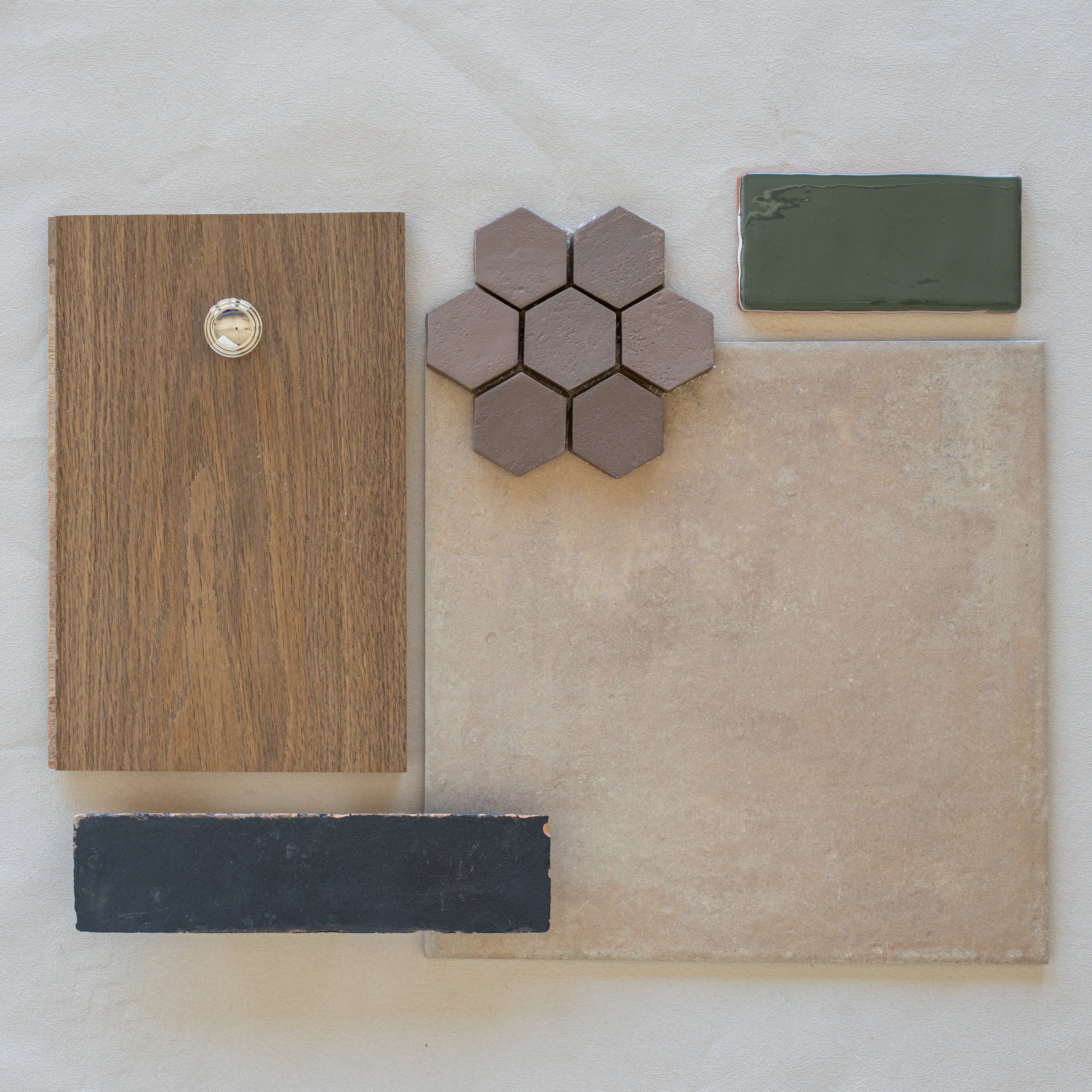 Flat lay of wood sample with metal knob, taupe hexagonal ceramic tiles, beige large tile, green rectangular tile, and black tile strip on fabric