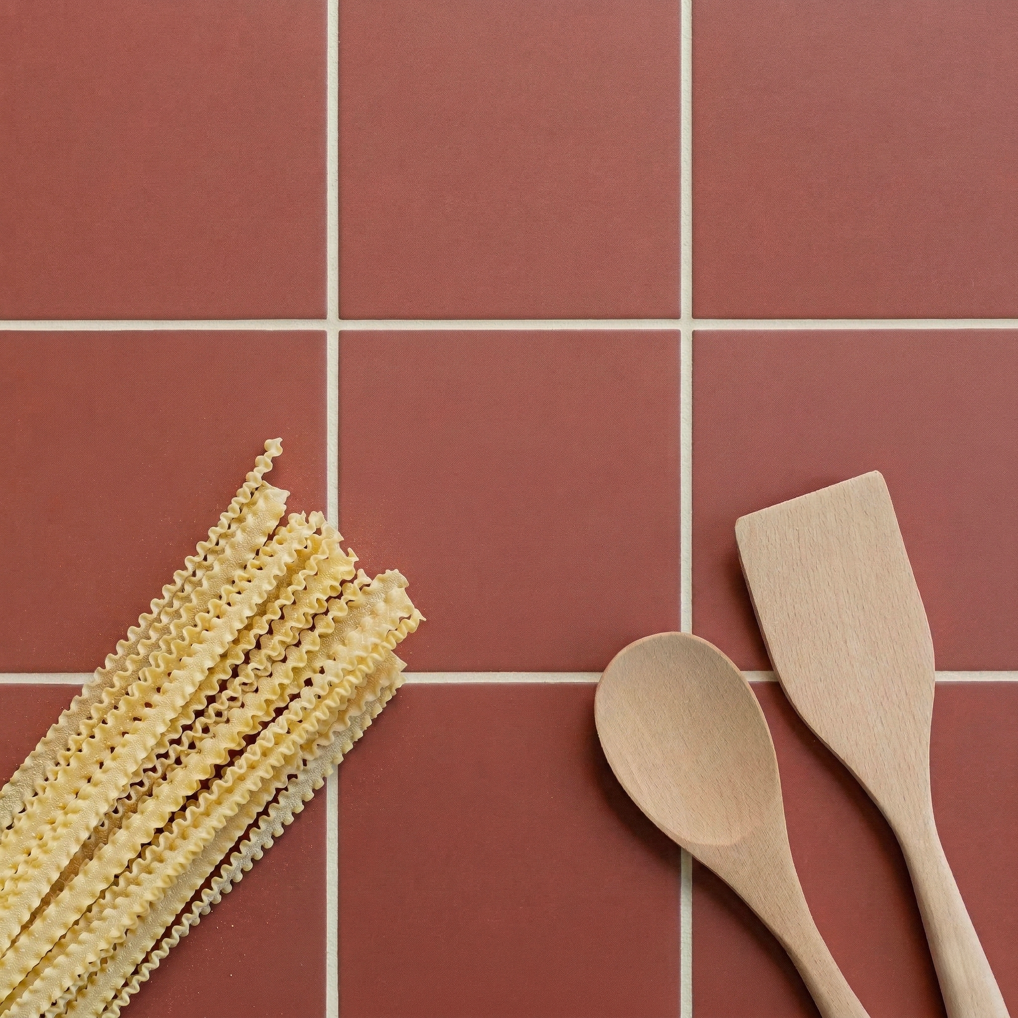 Close-up of terracotta tiles with wooden cooking utensils and uncooked pasta on the surface