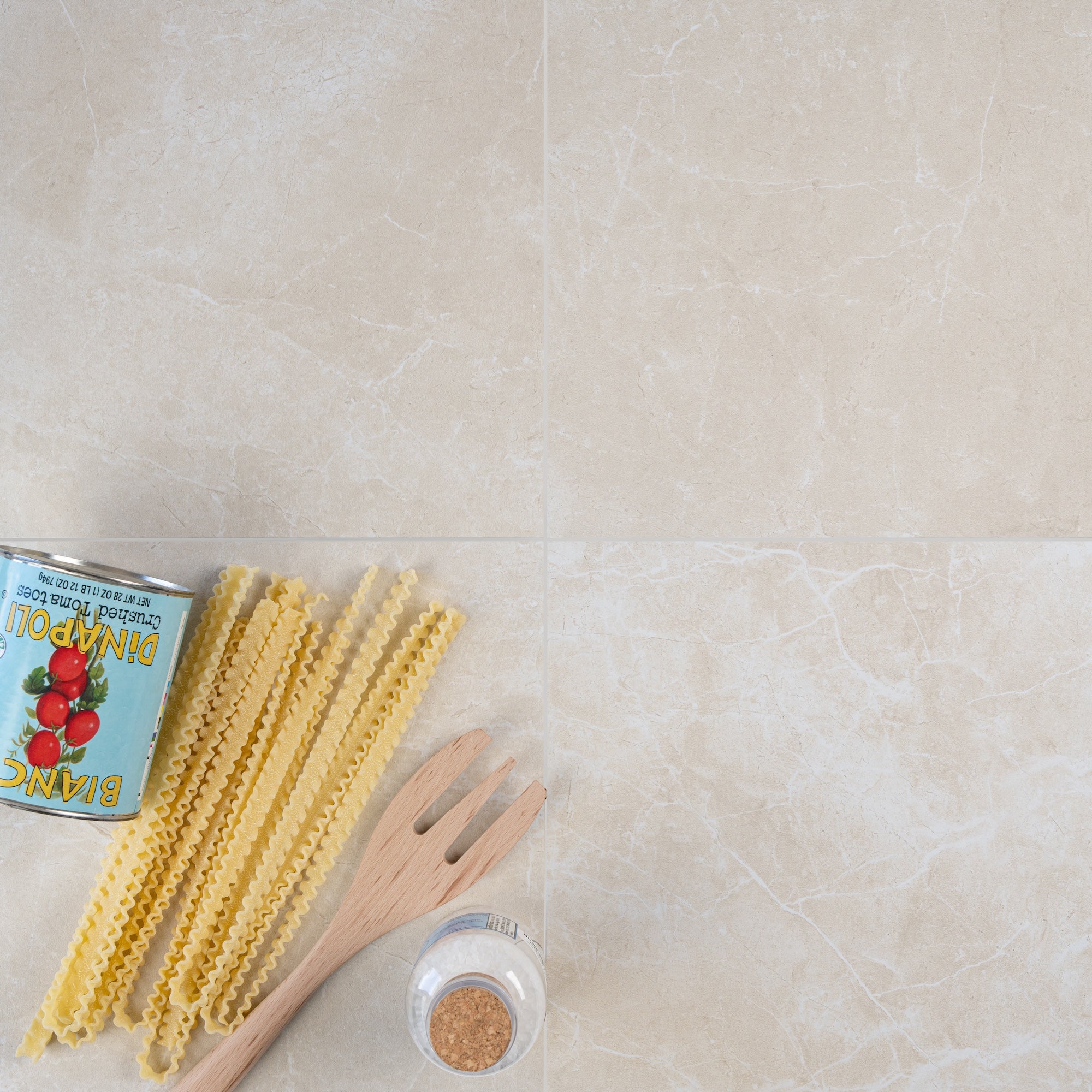 Four large beige porcelain tiles with subtle white veining and kitchen utensils on a neutral surface