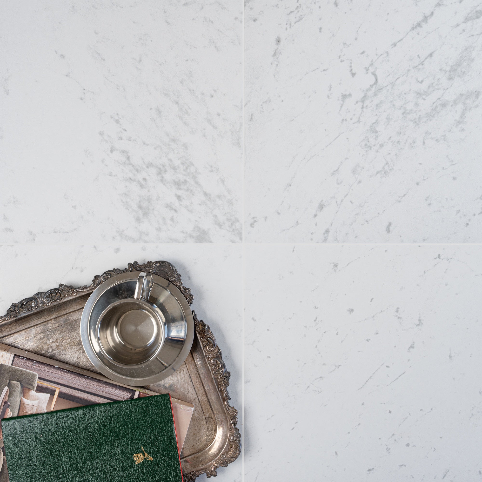Square porcelain tiles with subtle grey marble-like veining beside a vintage silver tray holding a cup and green book
