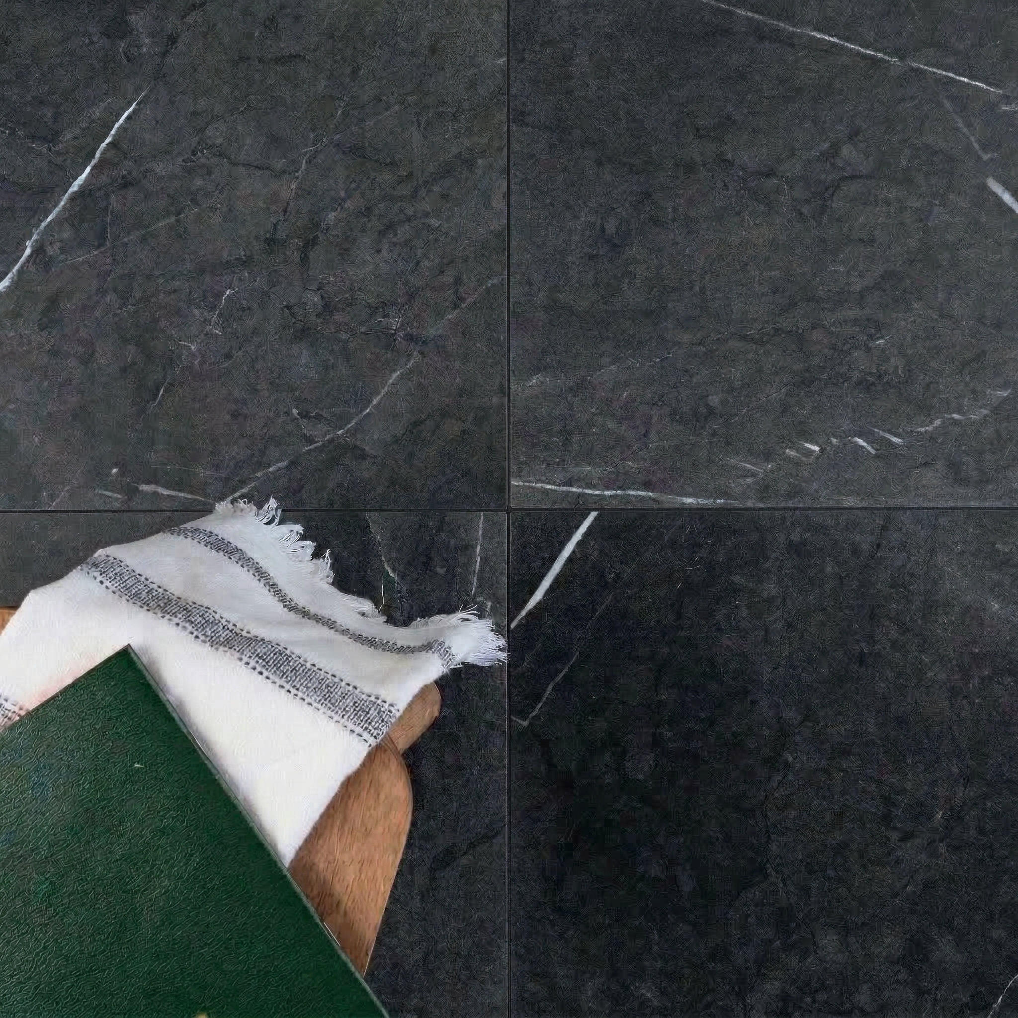 Dark charcoal ceramic tiles with subtle white veining arranged in a grid near a striped cloth and green book corner
