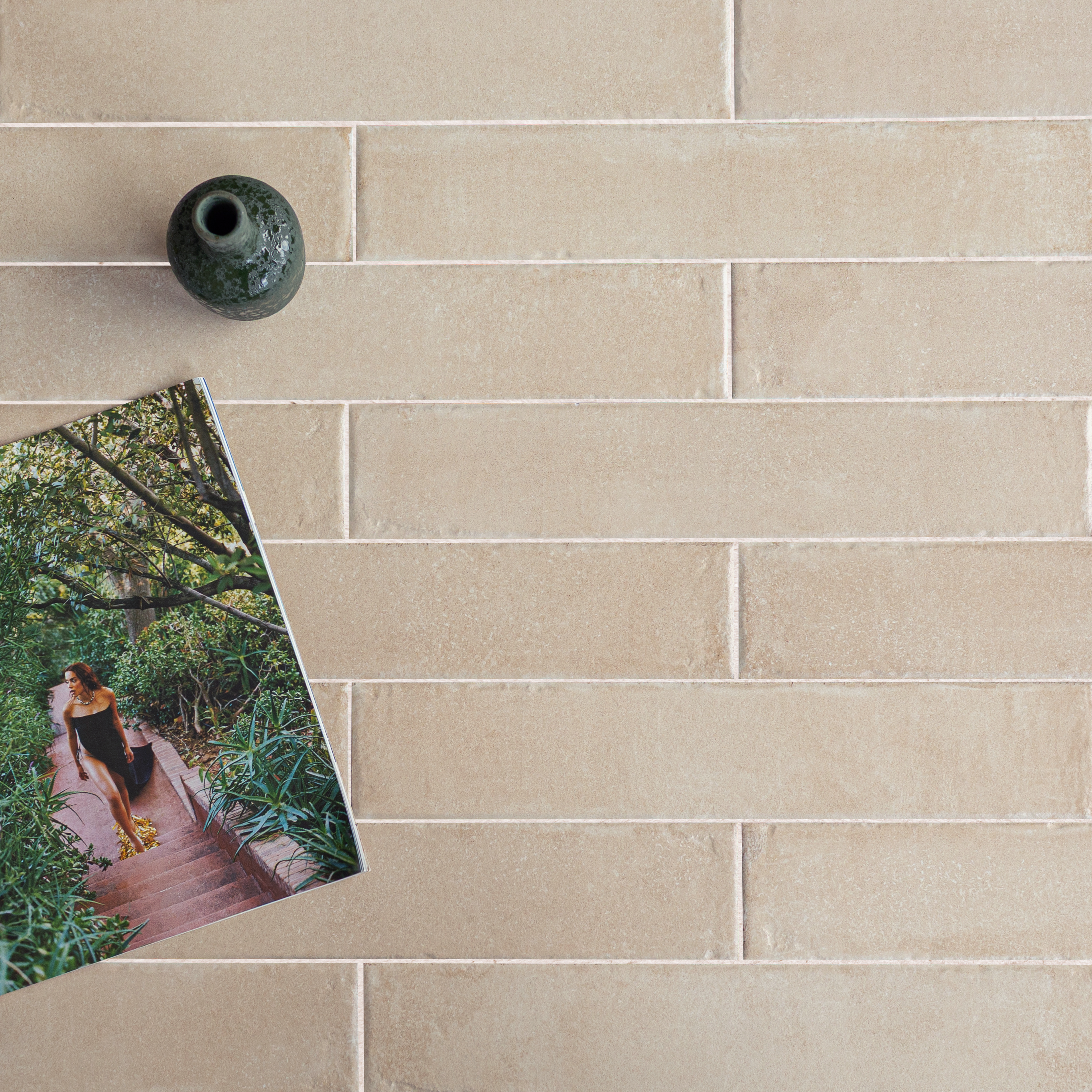 Beige rectangular ceramic tiles arranged in a staggered pattern with a green vase and an open magazine showing a woman outdoors