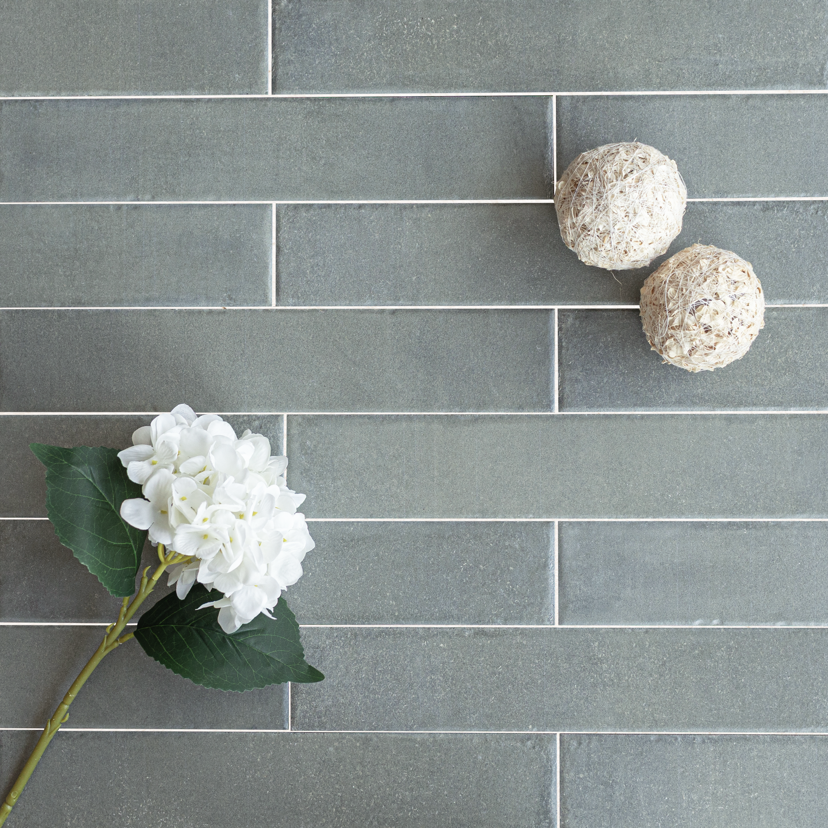 Soft green rectangular tiles laid in a horizontal staggered pattern with a white flower and two textured decorative spheres