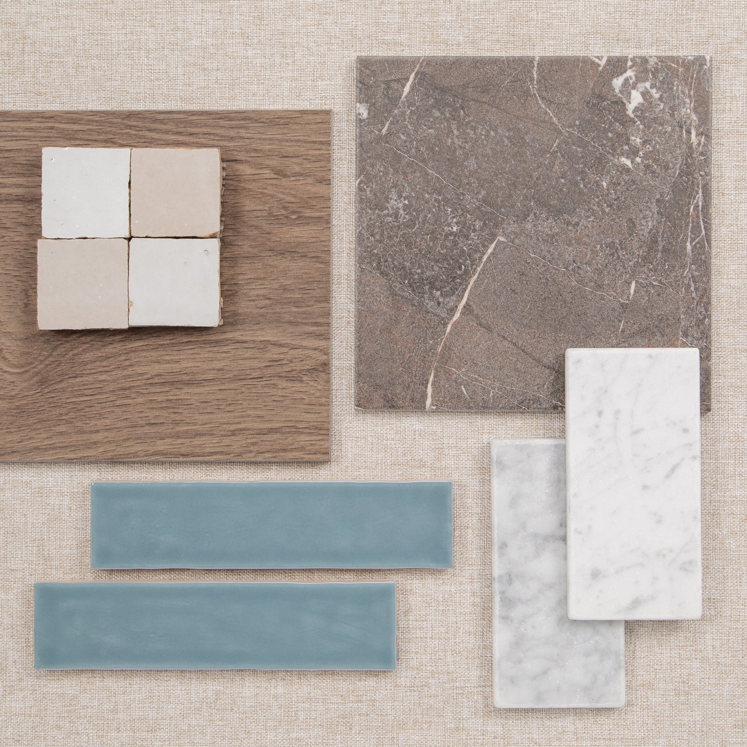 Flat lay of tile samples in white, blue, and stone finishes beside a wood flooring sample