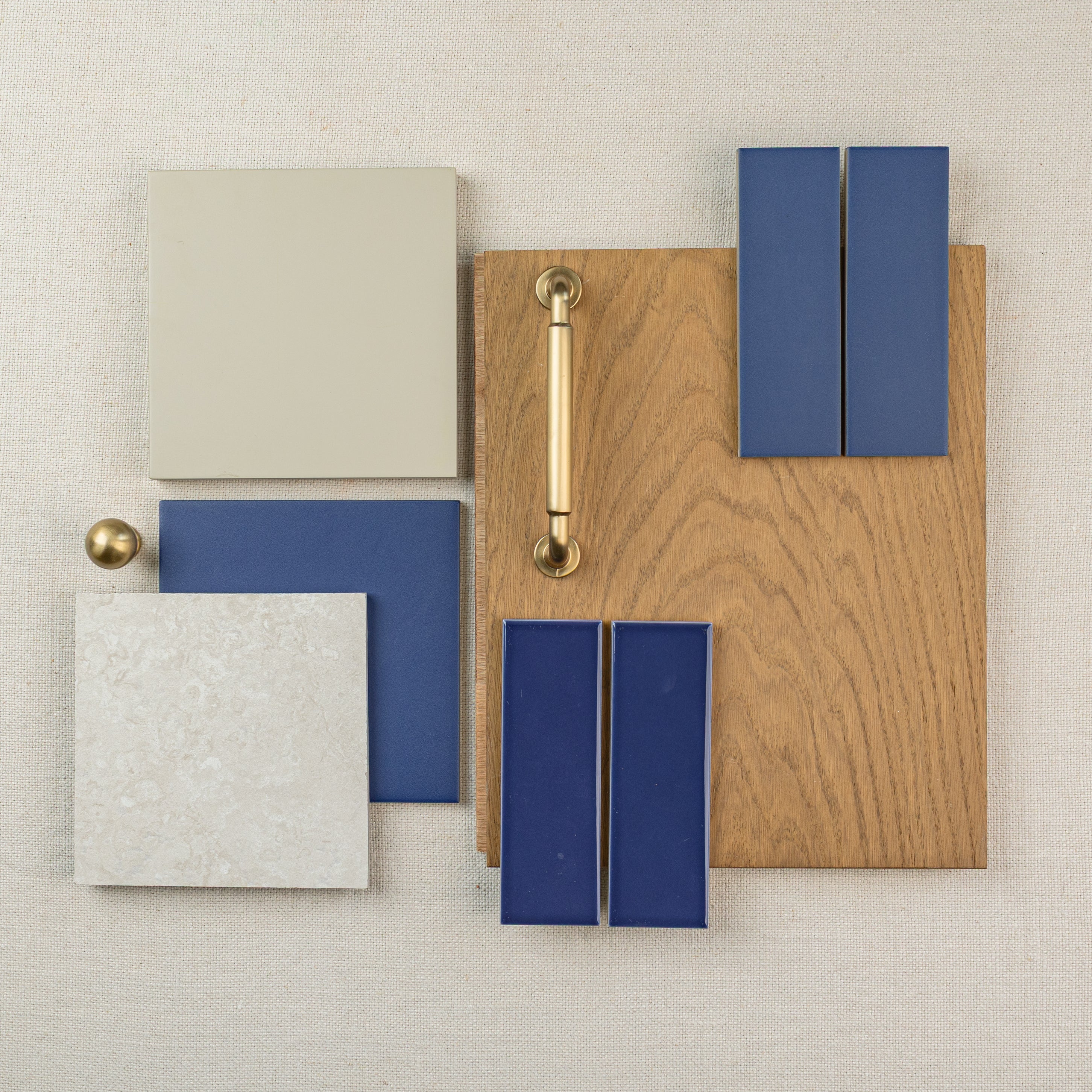 Wood board with brass handle, blue rectangular tiles, beige and light gray square tiles, and a brass knob on fabric background