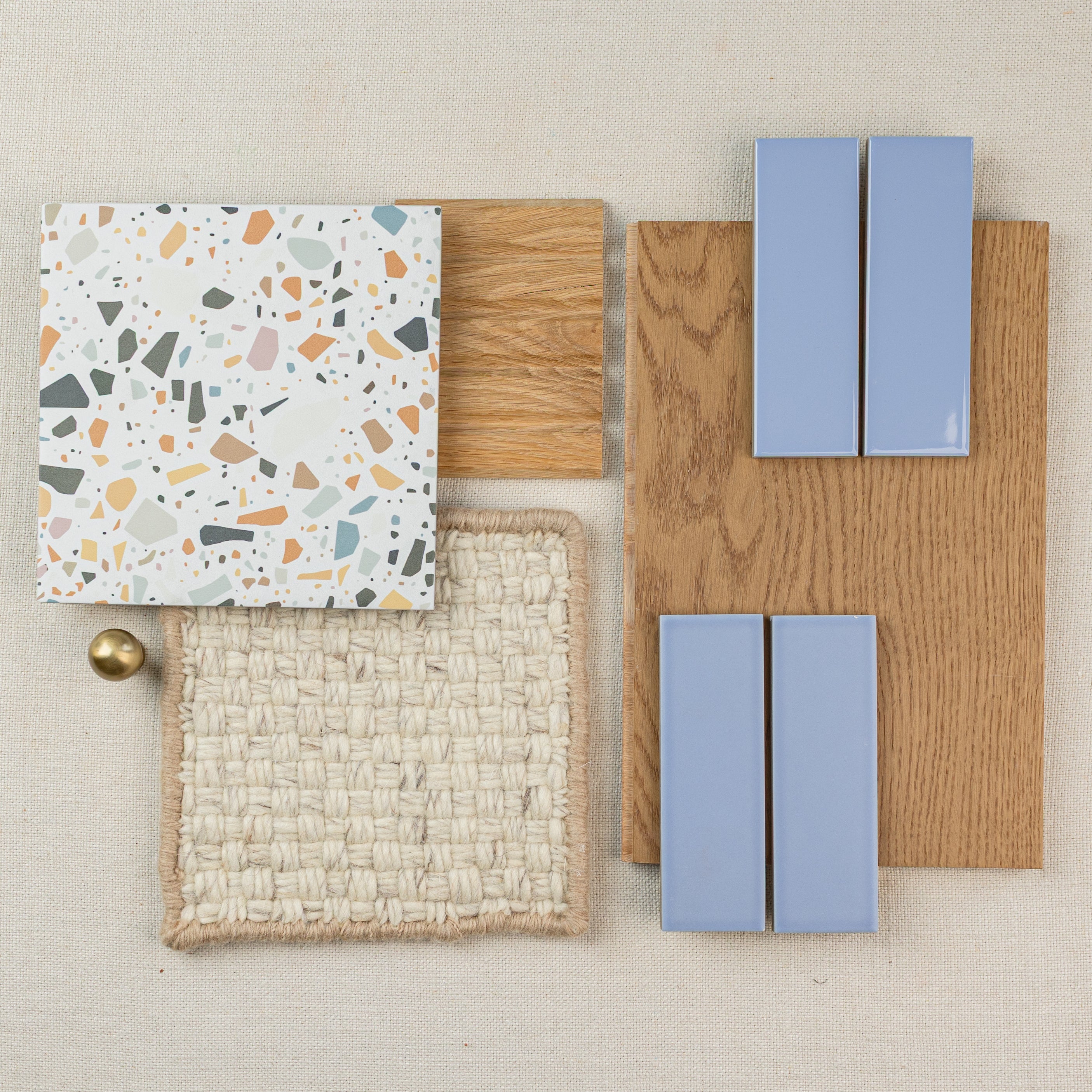 Terrazzo tile, woven fabric swatch, oak wood samples, and blue rectangular ceramic tiles arranged on neutral fabric background.
