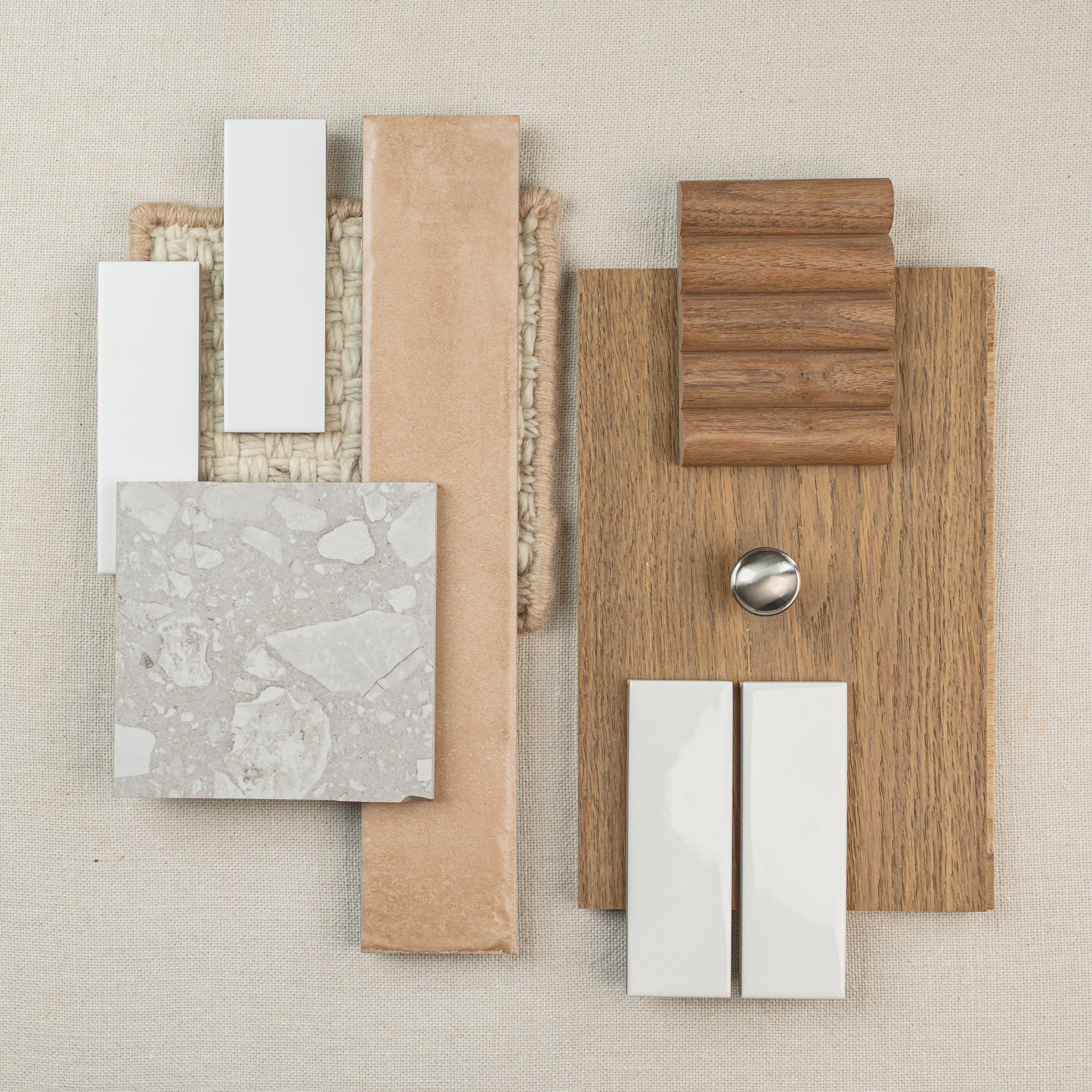 Assortment of tile samples, wood textures, and metal hardware arranged on neutral fabric background