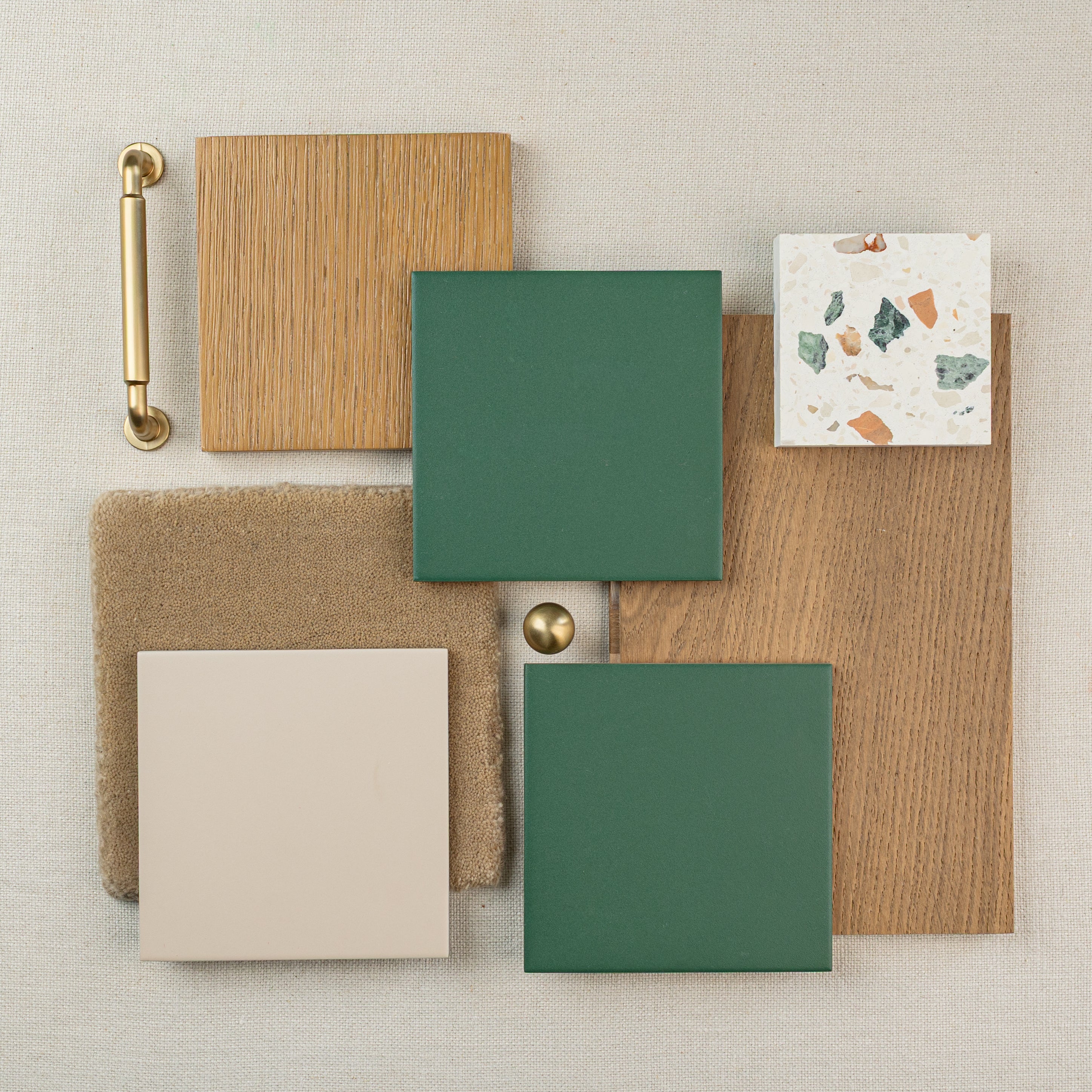 Square green tiles, wood samples, beige fabric, terrazzo tile, brass handle, and brass knob on neutral background