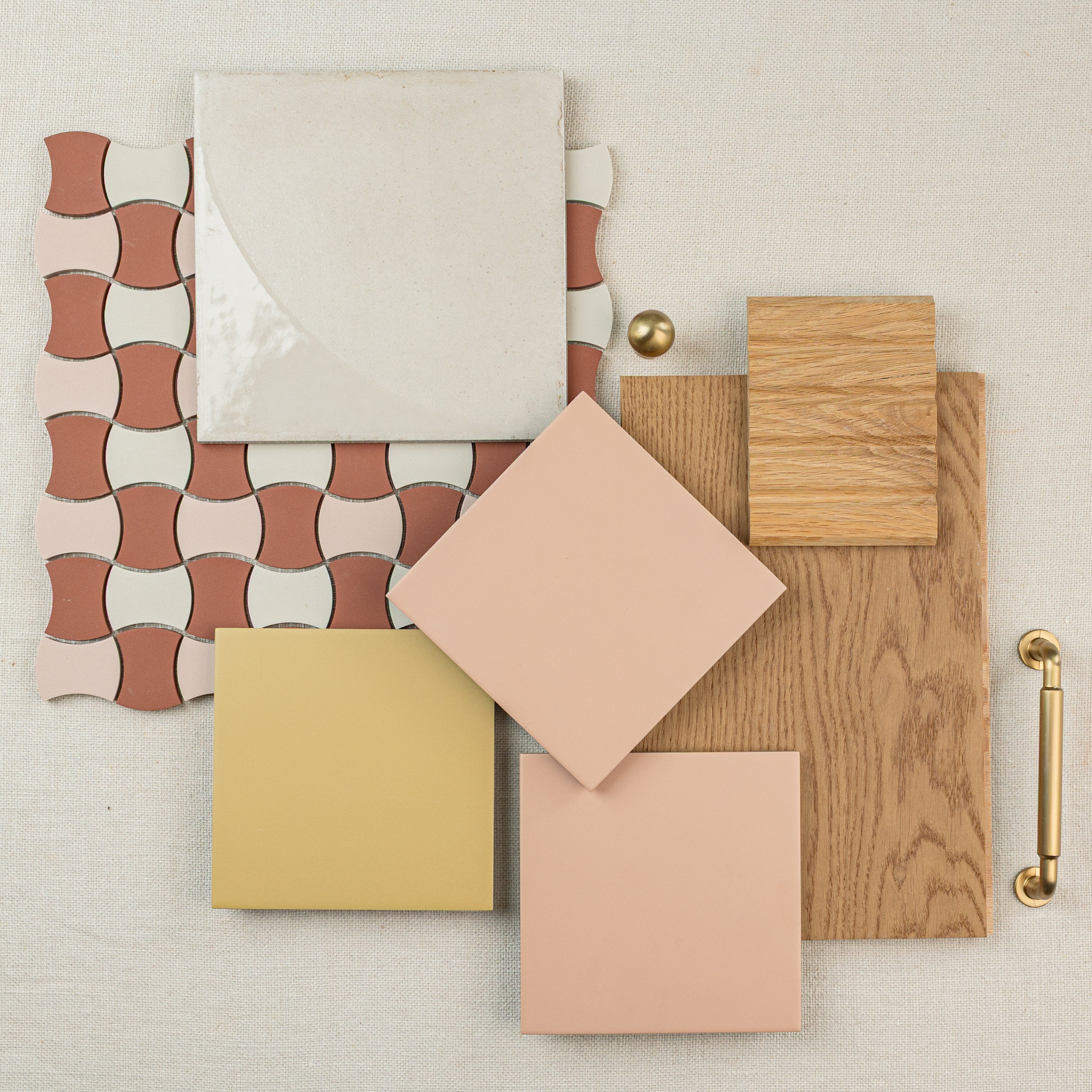 Assortment of ceramic tile samples and wood flooring swatches arranged on a neutral fabric background with a brass handle nearby