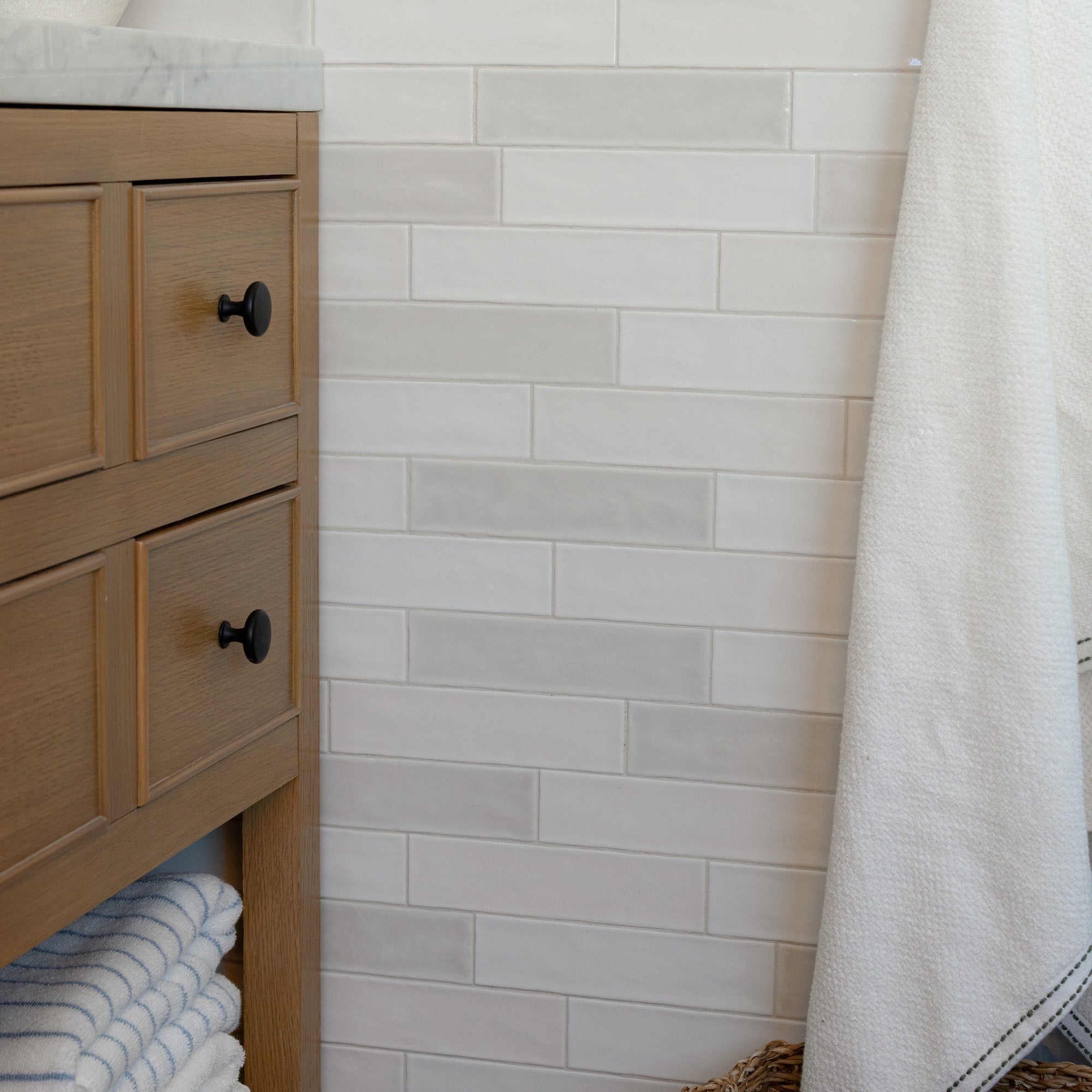 White subway tile wall beside a wood bathroom vanity and hanging towel