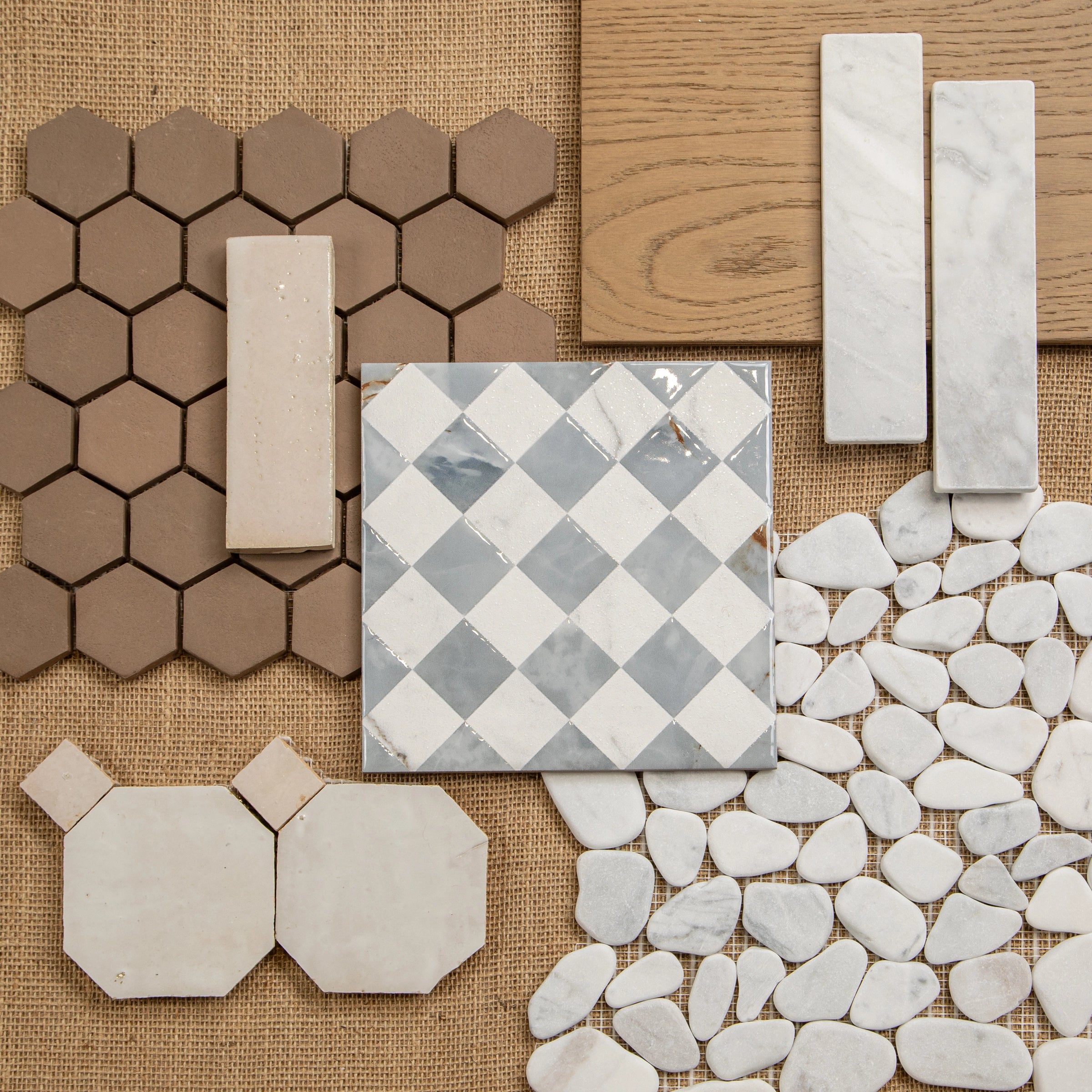 Collection of hexagonal, rectangular, checkered, pebble, and wood tile samples on a textured natural fabric background