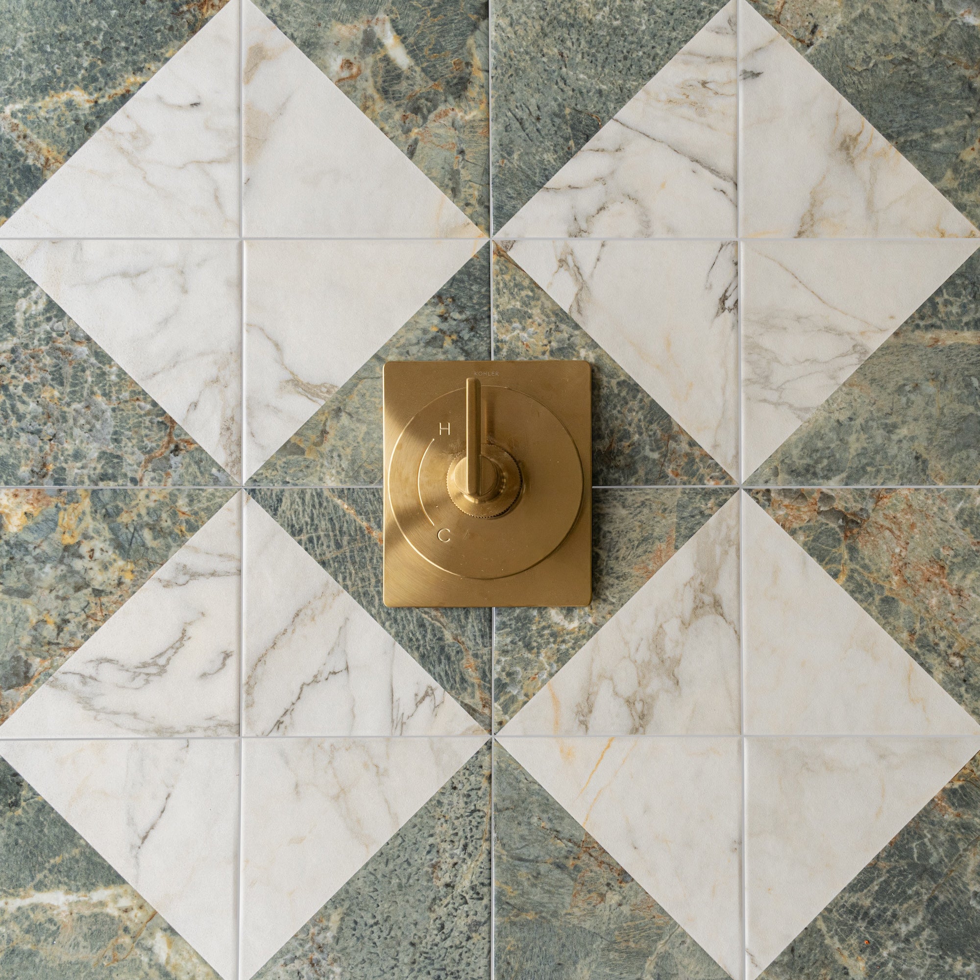 Matte white marble diamond tiles paired with textured green stone tiles and a square brass shower control knob
