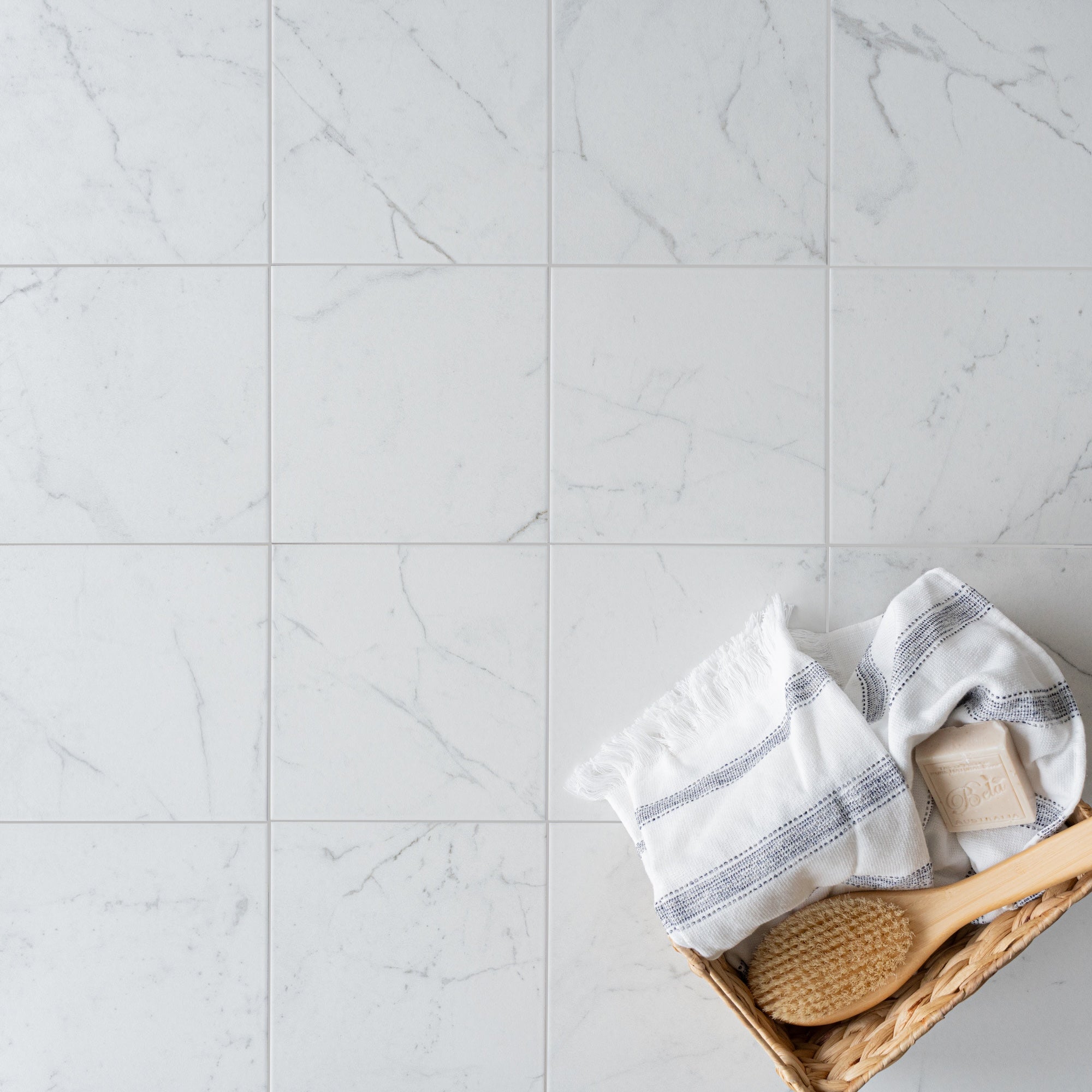 Soft white porcelain tiles with subtle gray veining next to a woven basket holding a striped towel and wooden brush
