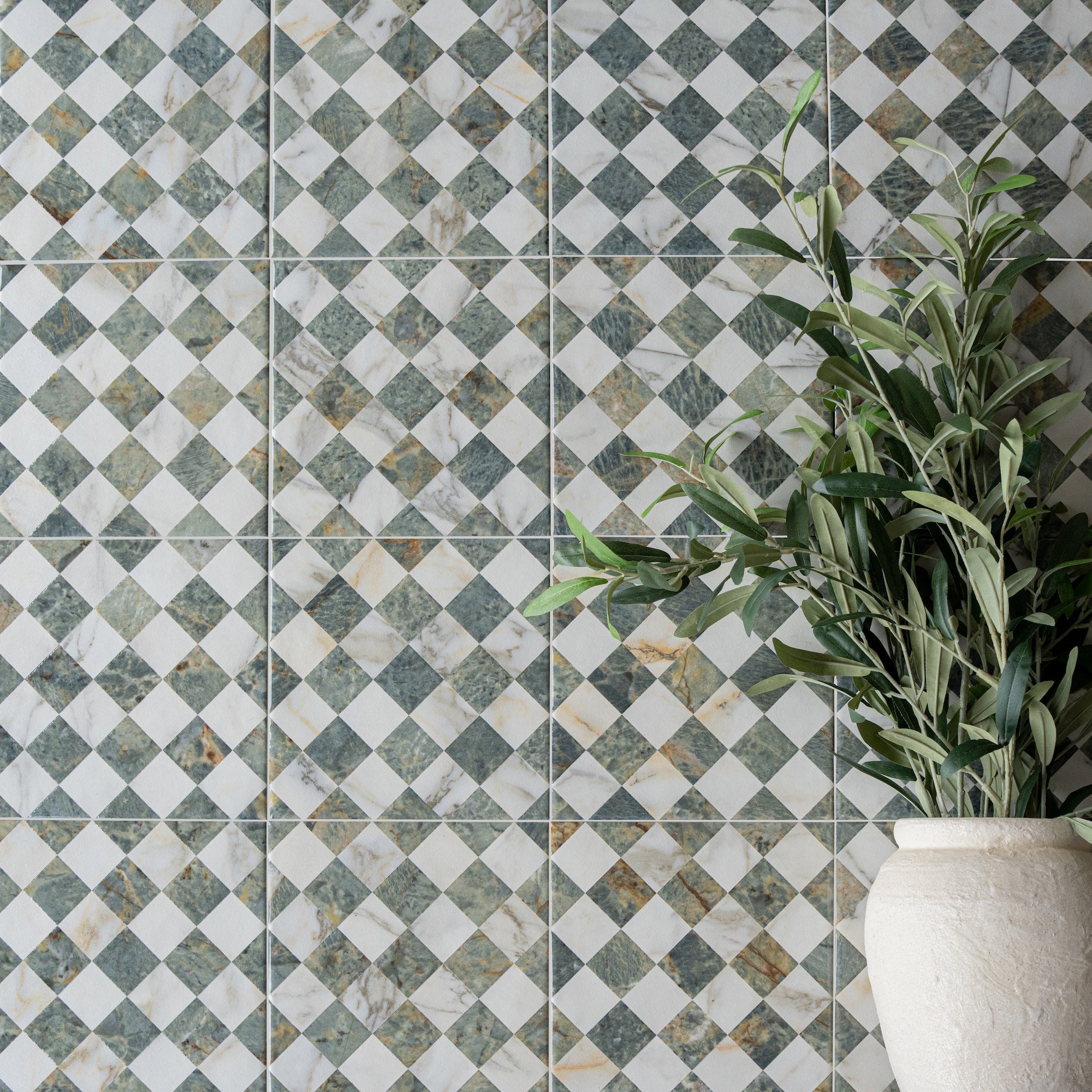 Ceramic wall tiles with green and white diamond pattern next to a textured white vase holding leafy green branches