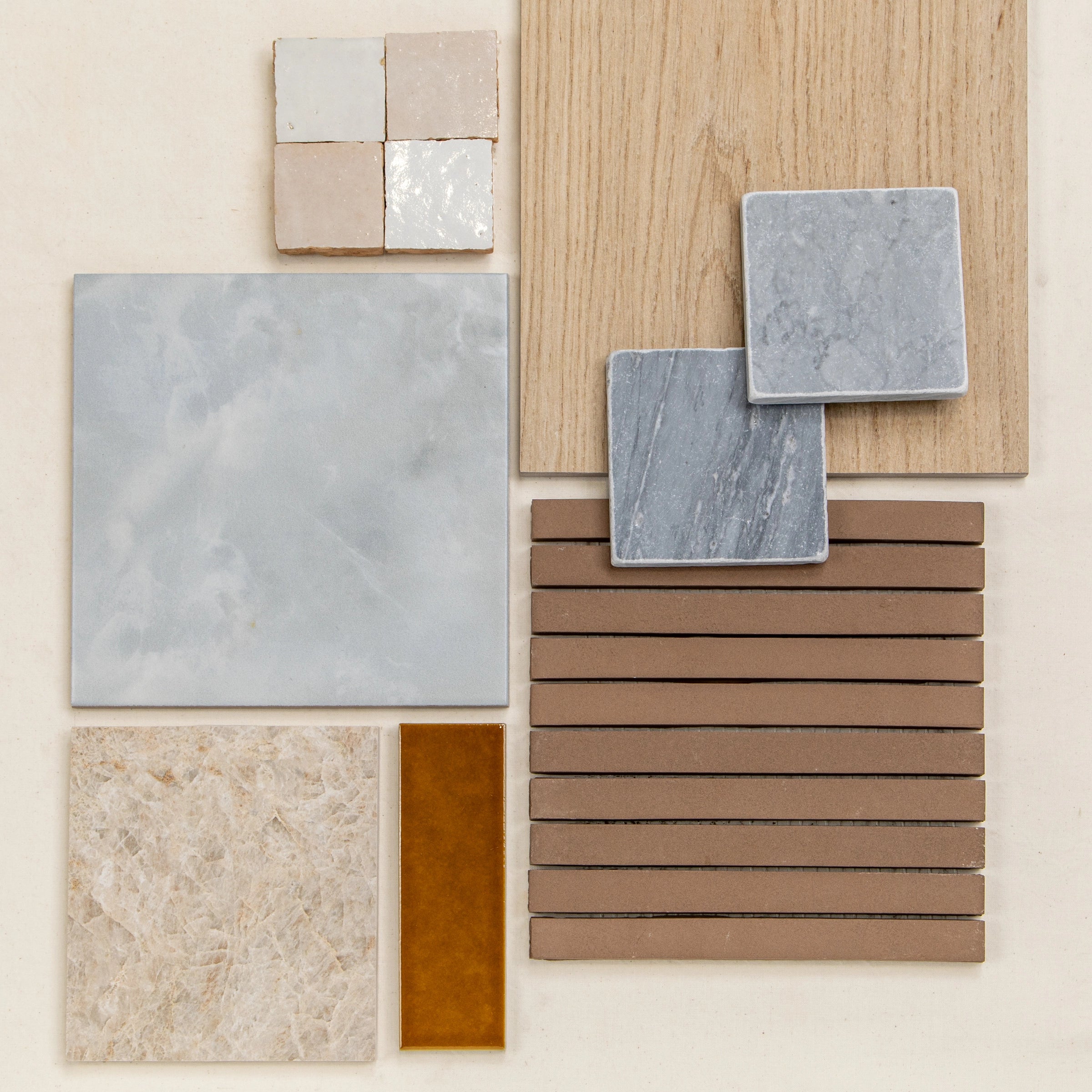 Collection of beige, gray, and wood-inspired ceramic and porcelain tile samples arranged on a neutral surface