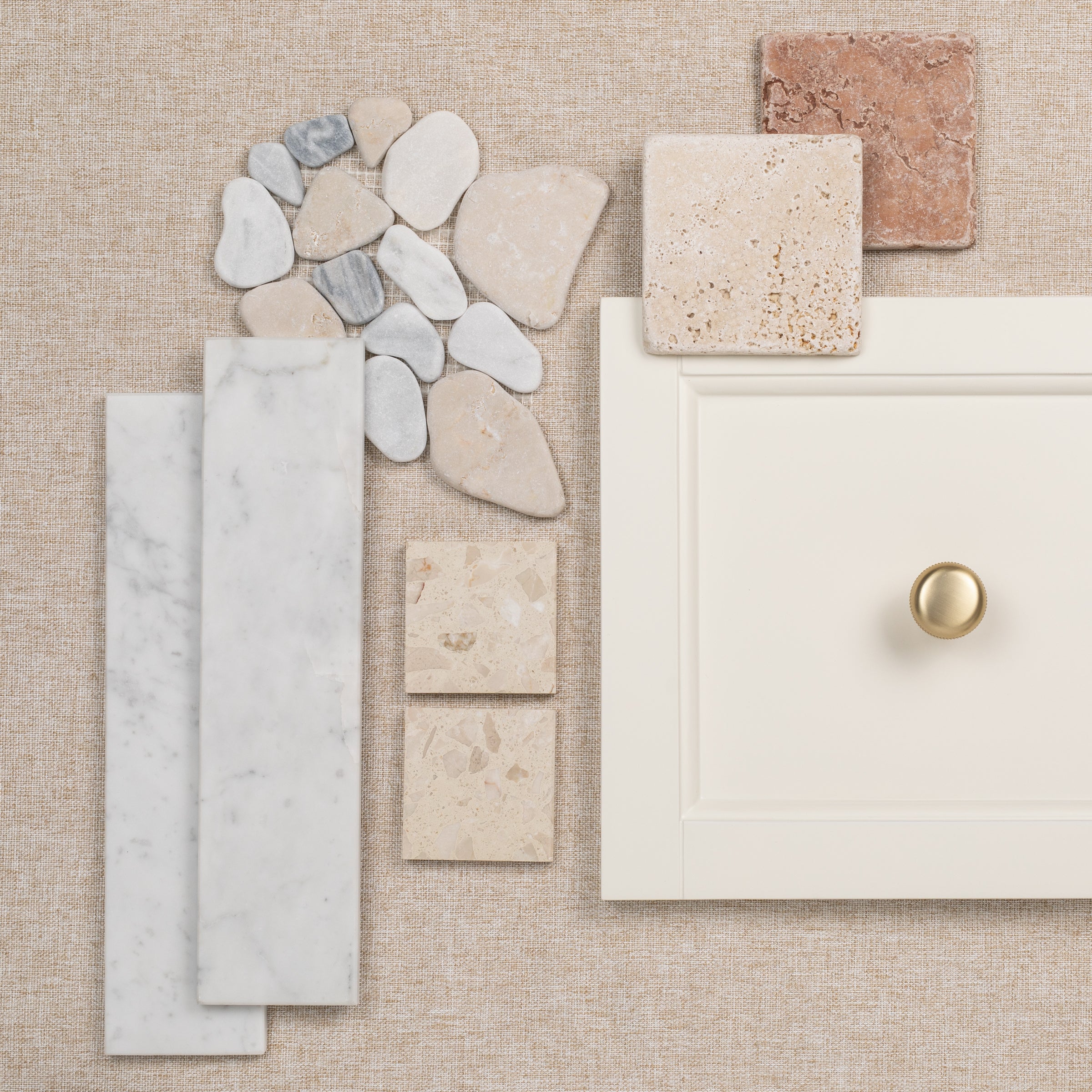 Various neutral-toned tile samples and a cream cabinet drawer front with a gold knob on a textured background
