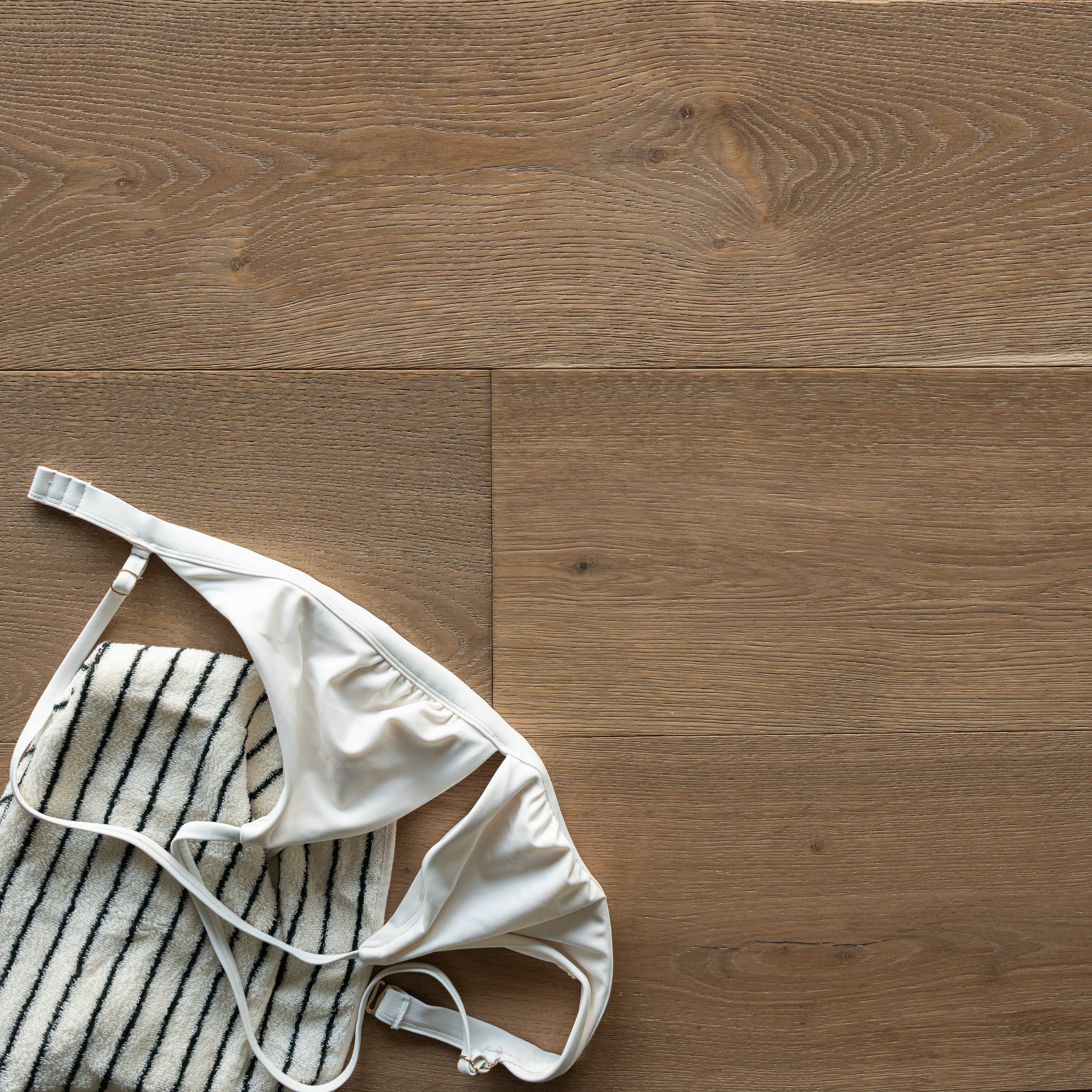 Light oak engineered wood flooring with subtle grain texture beneath a white bra and striped fabric piece laid casually